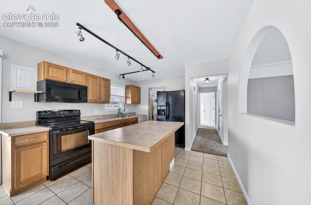 Kitchen featuring wood-finish cabinetry, black appliances, track lighting, and a center island