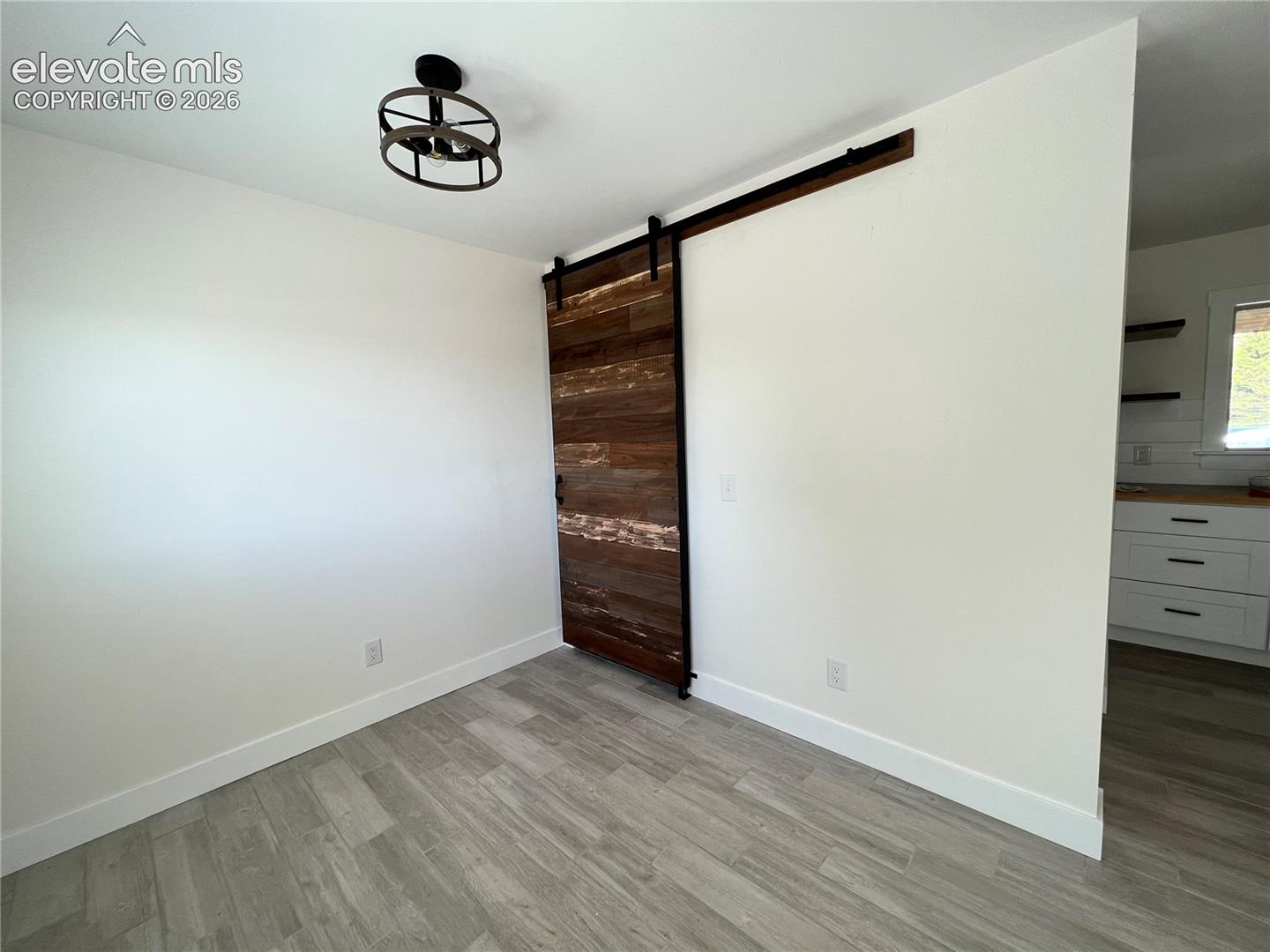 Wood-finish flooring, accent barn door with dark hardware, and a semi-flush mount ceiling fixture