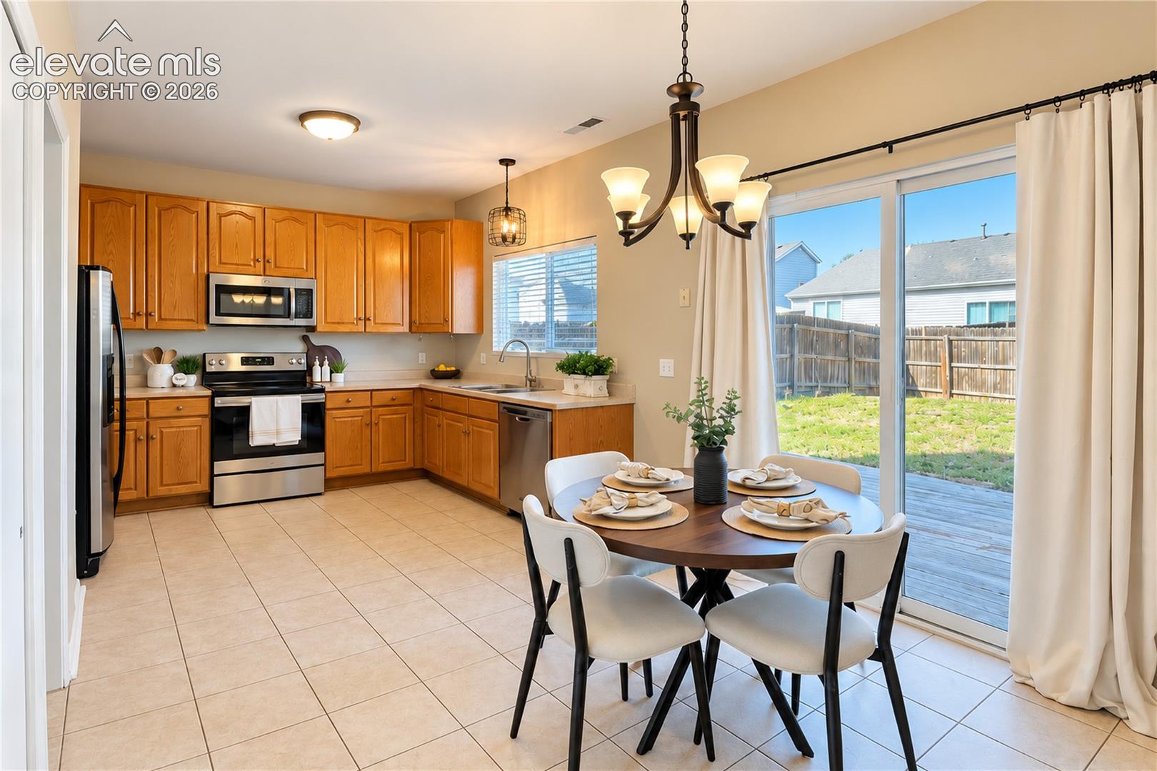 Kitchen featuring natural wood cabinetry, stainless steel appliances, ceramic tile flooring, a multi-arm chandelier, and sliding glass doors with direct exterior access