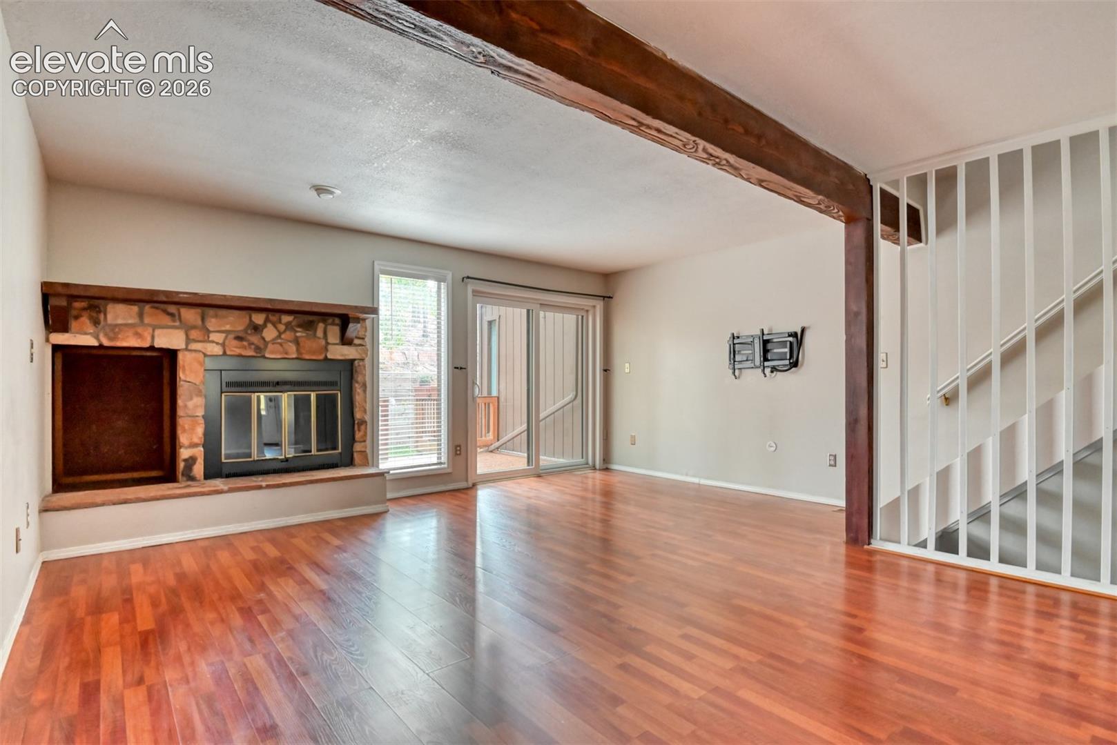 Stone-faced fireplace, wood-finish flooring, exposed wood beam, sliding glass door, and staircase with vertical balusters