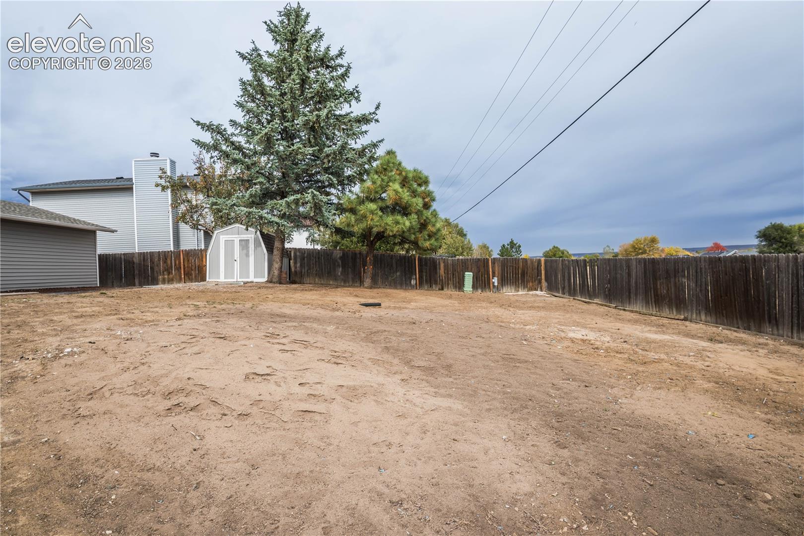 Backyard featuring a wood privacy fence, mature evergreen trees, and a detached storage shed