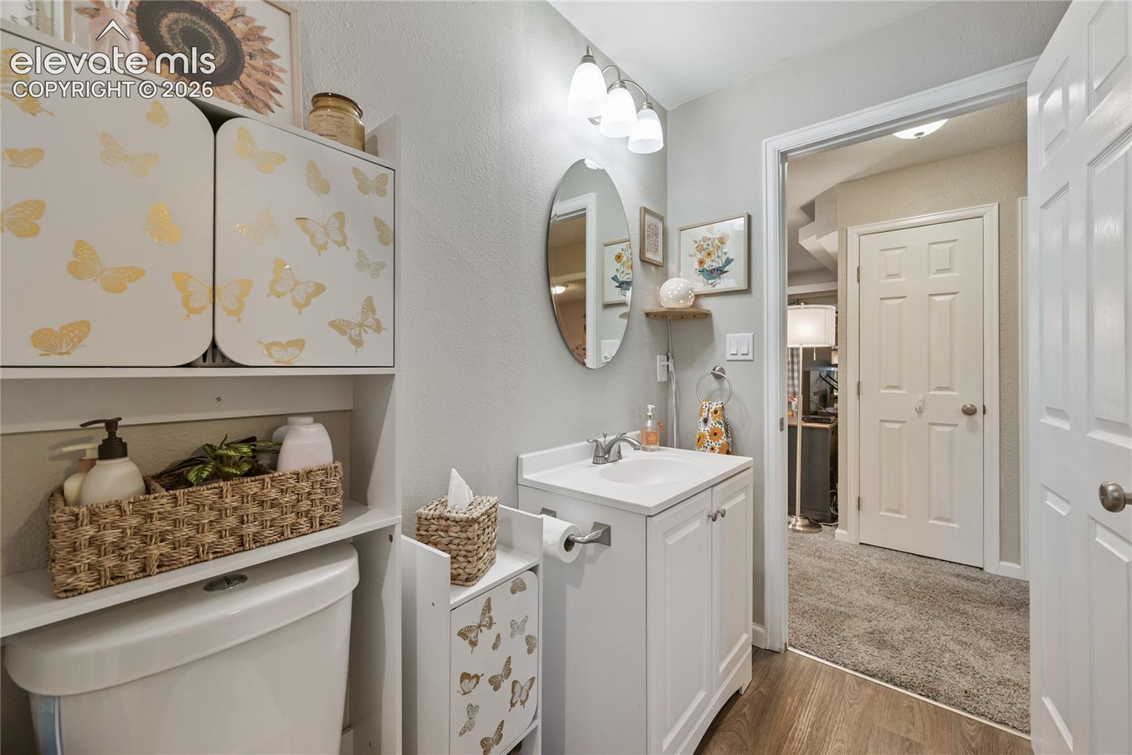 White vanity with an integrated countertop, oval wall-mounted mirror, three-light fixture, and wood-finish flooring