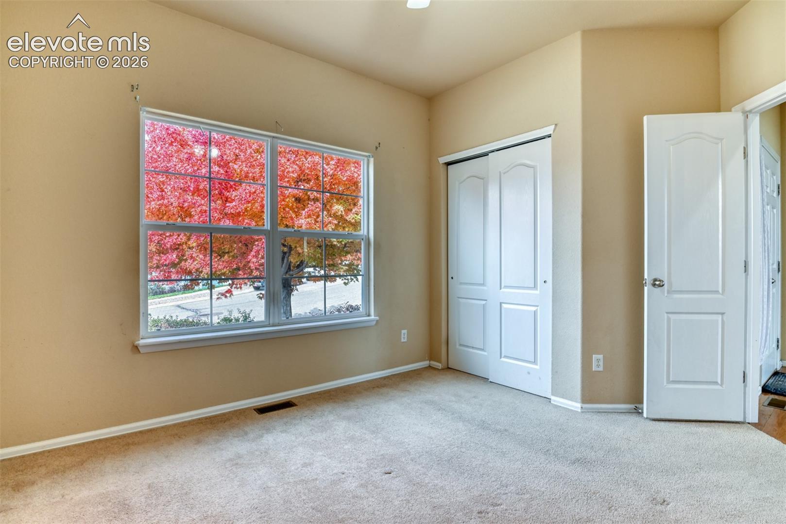Room featuring carpeting, dual-panel sliding closet doors, a multi-pane window, and an interior panel door