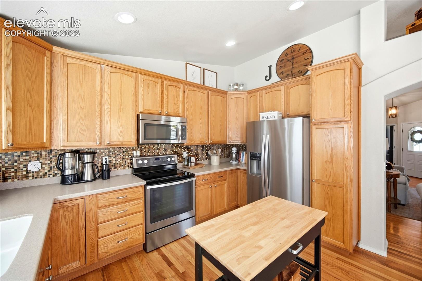 Kitchen featuring wood cabinetry, stainless steel appliances, mosaic tile backsplash, and wood-finish flooring