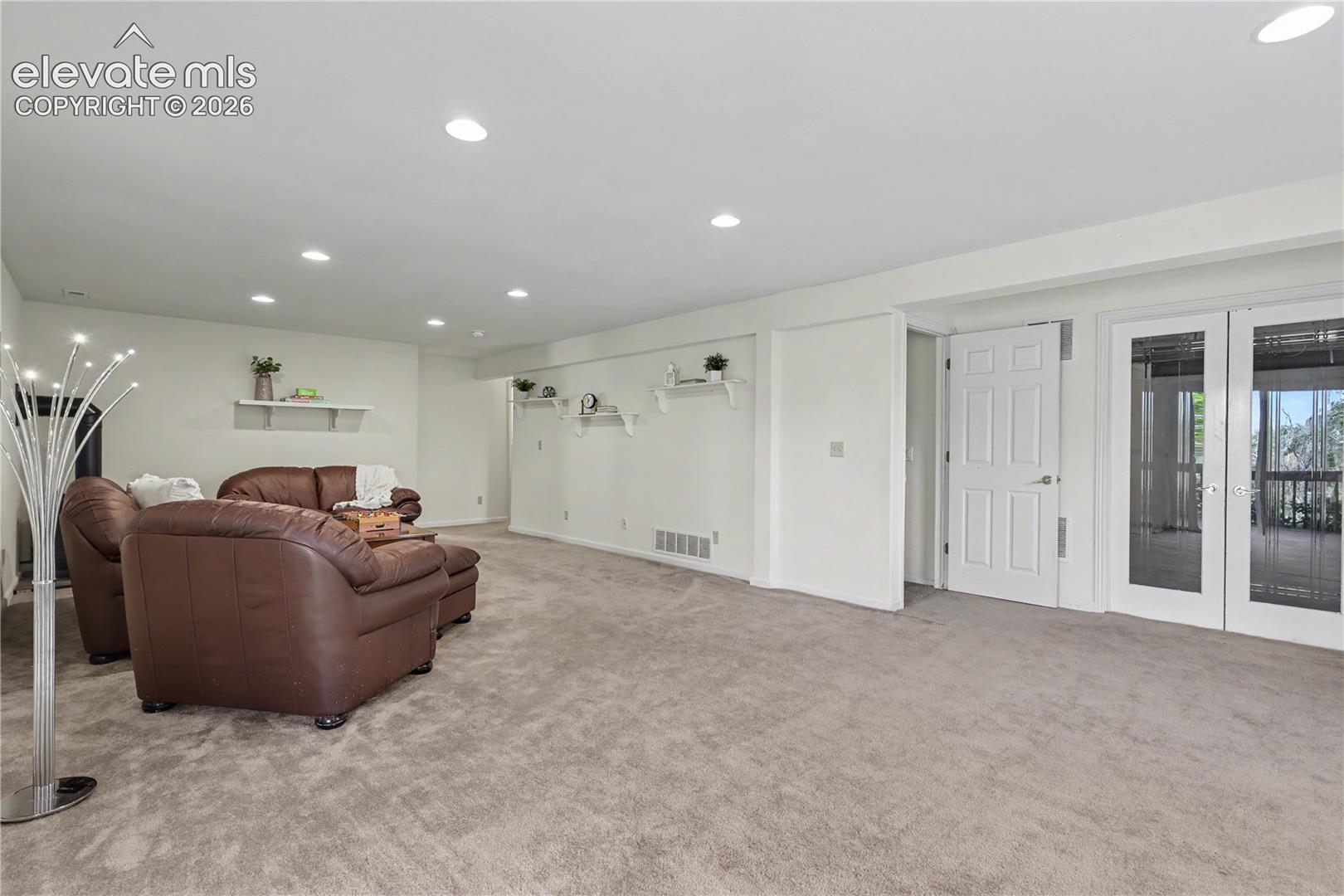 Spacious room featuring neutral carpeting, recessed lighting, white walls, built-in shelving, and double French doors with glass panels