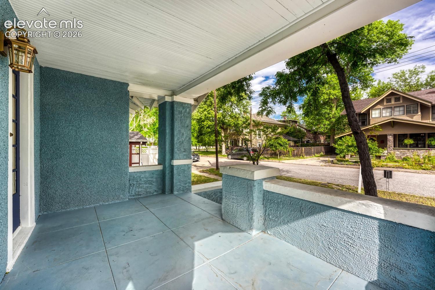 Covered front porch featuring textured stucco walls, square-cut tile flooring, a white paneled ceiling, and an exterior wall lantern