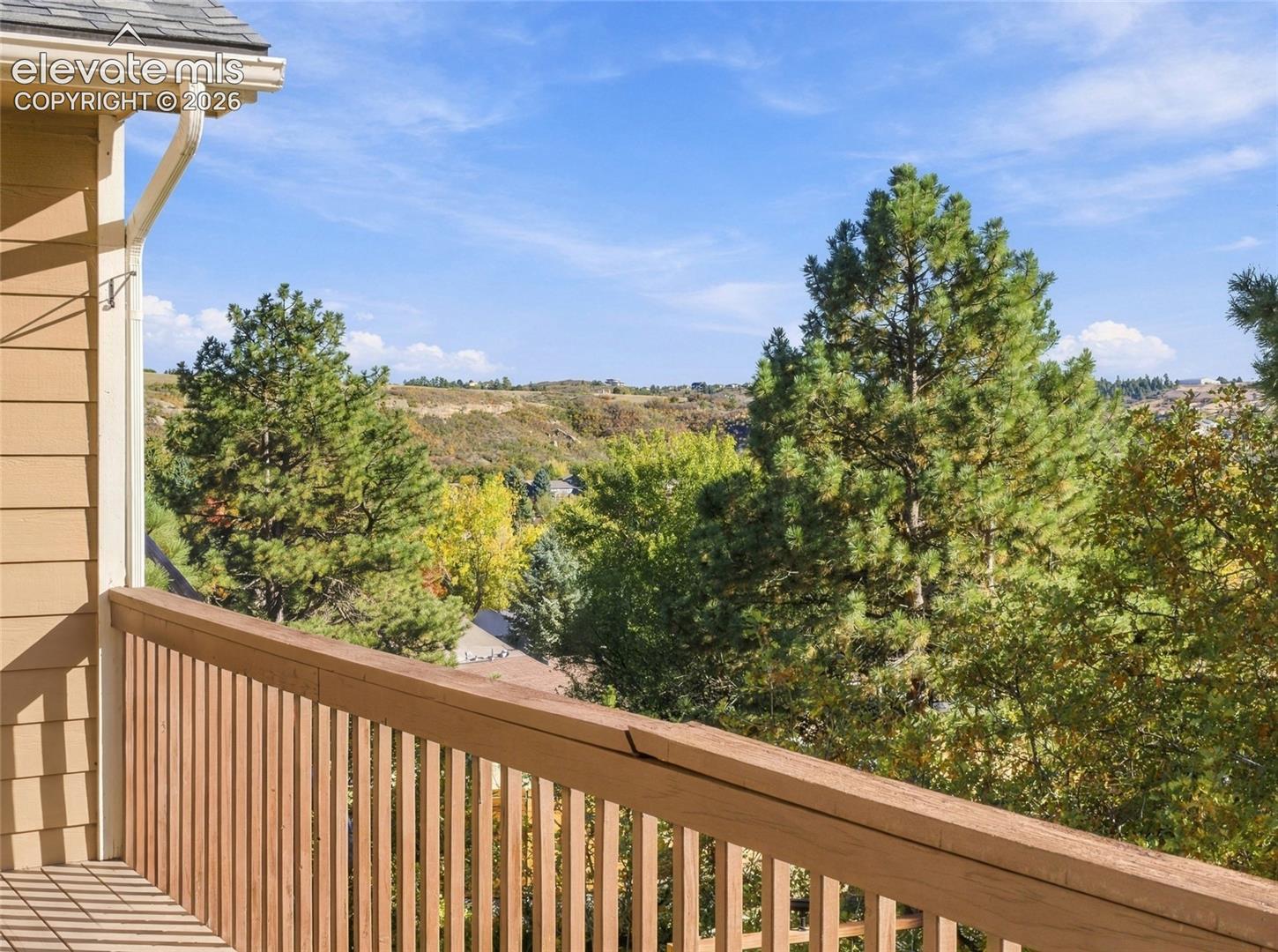 Elevated deck featuring wooden balustrades and horizontal siding, overlooking mature evergreen and deciduous trees