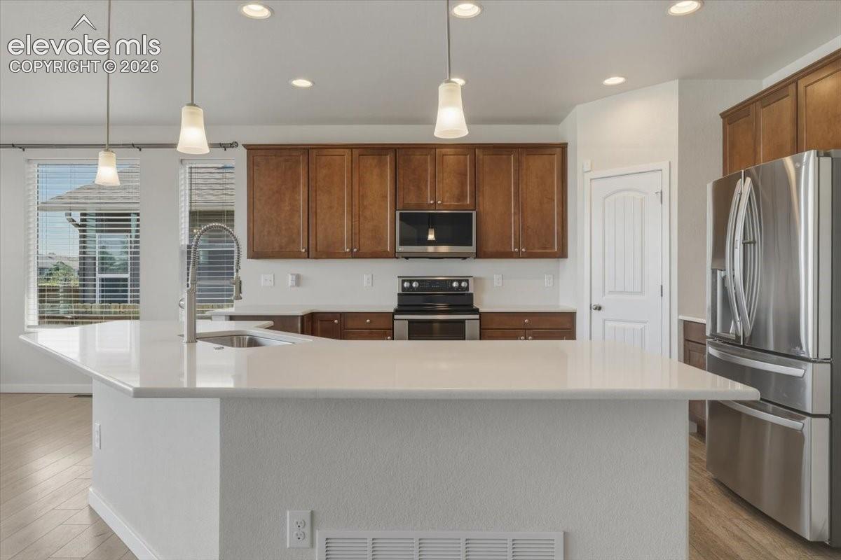 Kitchen featuring a large central island with a sink and pendant lighting, wood-finish flooring, stainless steel appliances, and wood cabinetry