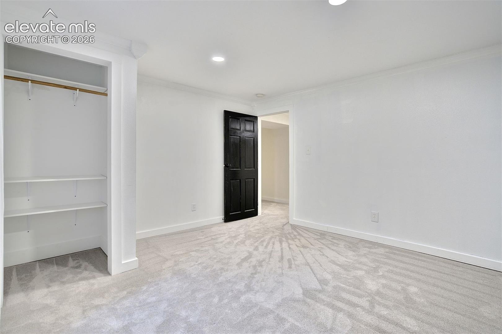 Interior room featuring wall-to-wall carpeting, recessed ceiling lighting, a built-in closet with integrated shelving, and a contrasting black paneled door