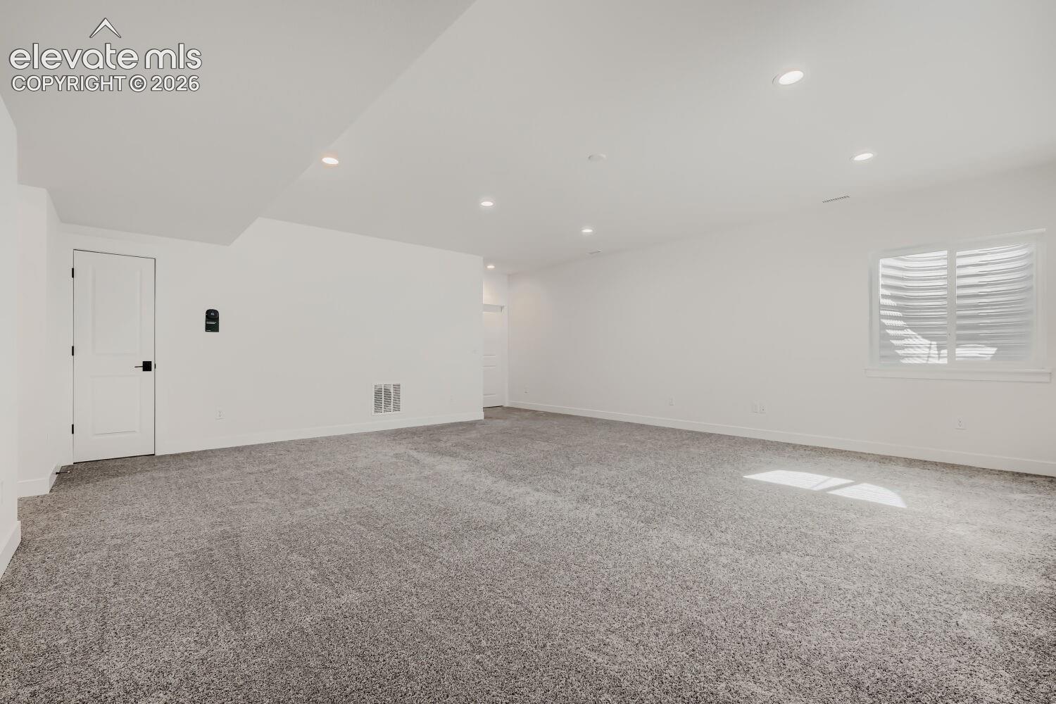 Expansive room featuring recessed lighting, a window with horizontal blinds, and a paneled interior door with matte black hardware