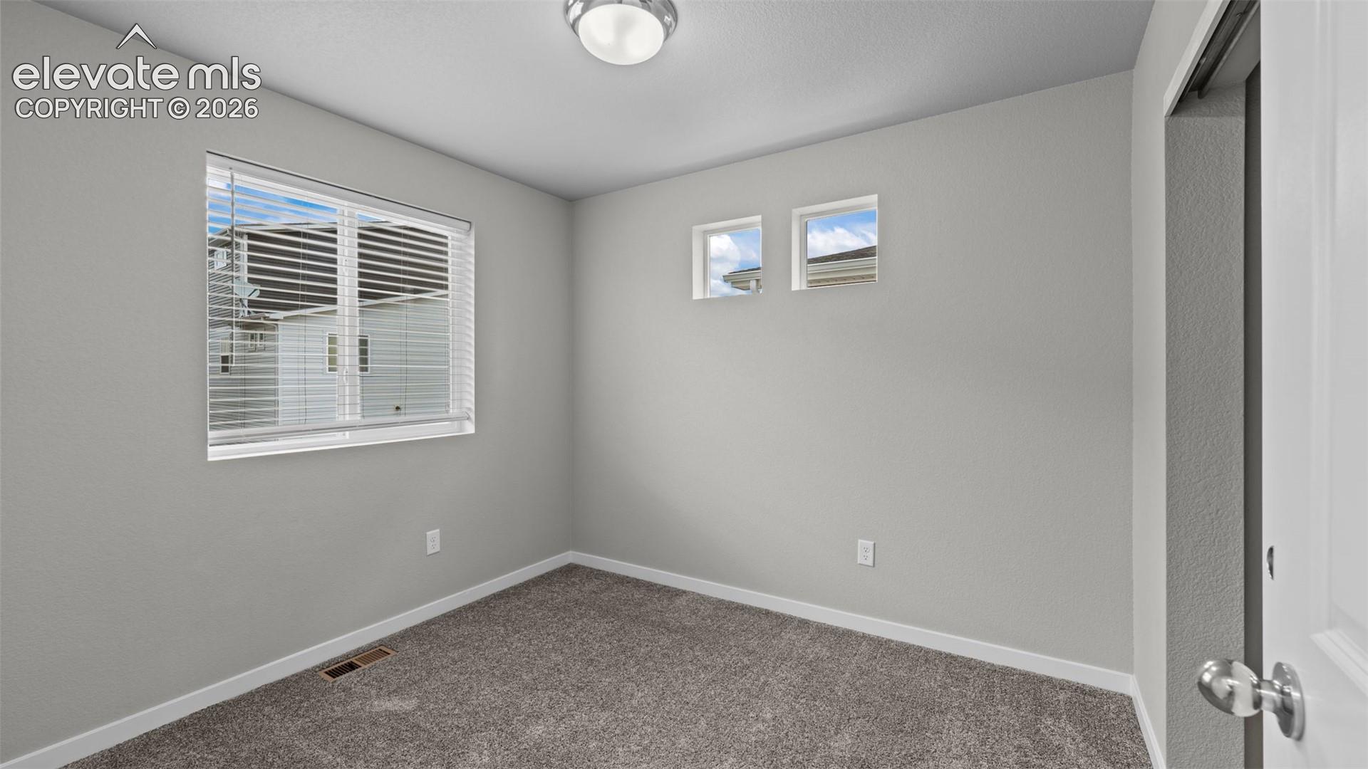 Neutral-toned interior room featuring wall-to-wall carpeting, a multi-pane window with horizontal blinds, two high-set accent windows, and a central ceiling-mounted light fixture