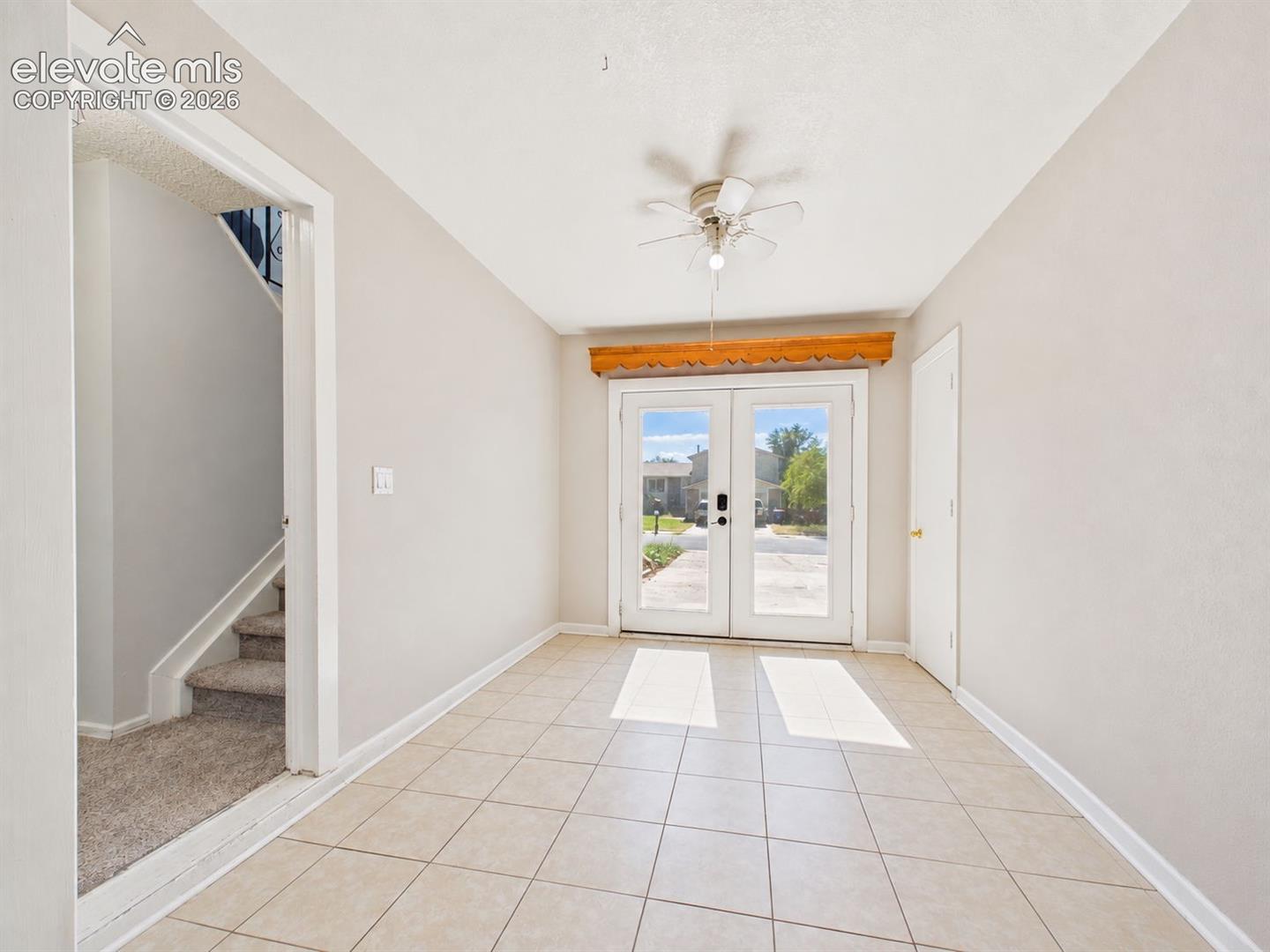 Front Entry / Flex Space – Bright tiled entry area features glass-paneled double doors, a ceiling fan, and convenient access to the home's split-level staircase.