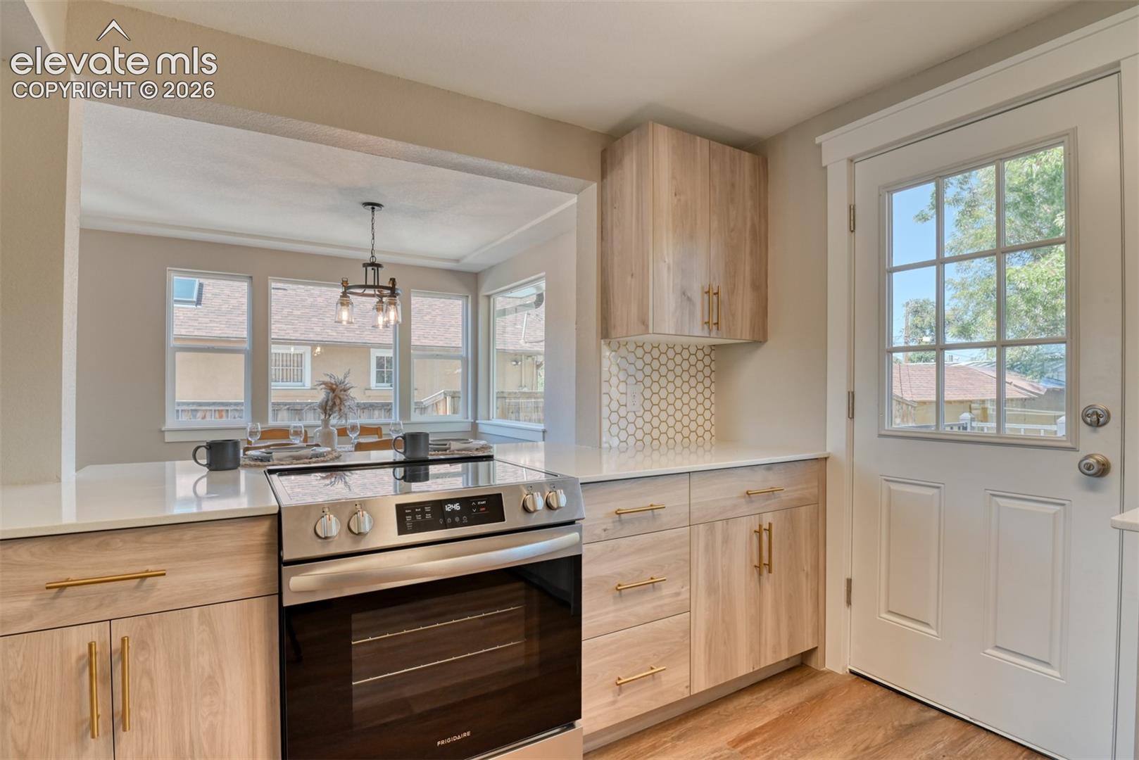 Integrated kitchen featuring a stainless steel range, light wood-finish cabinetry, white countertops, hexagon tile backsplash, and wood-finish flooring
