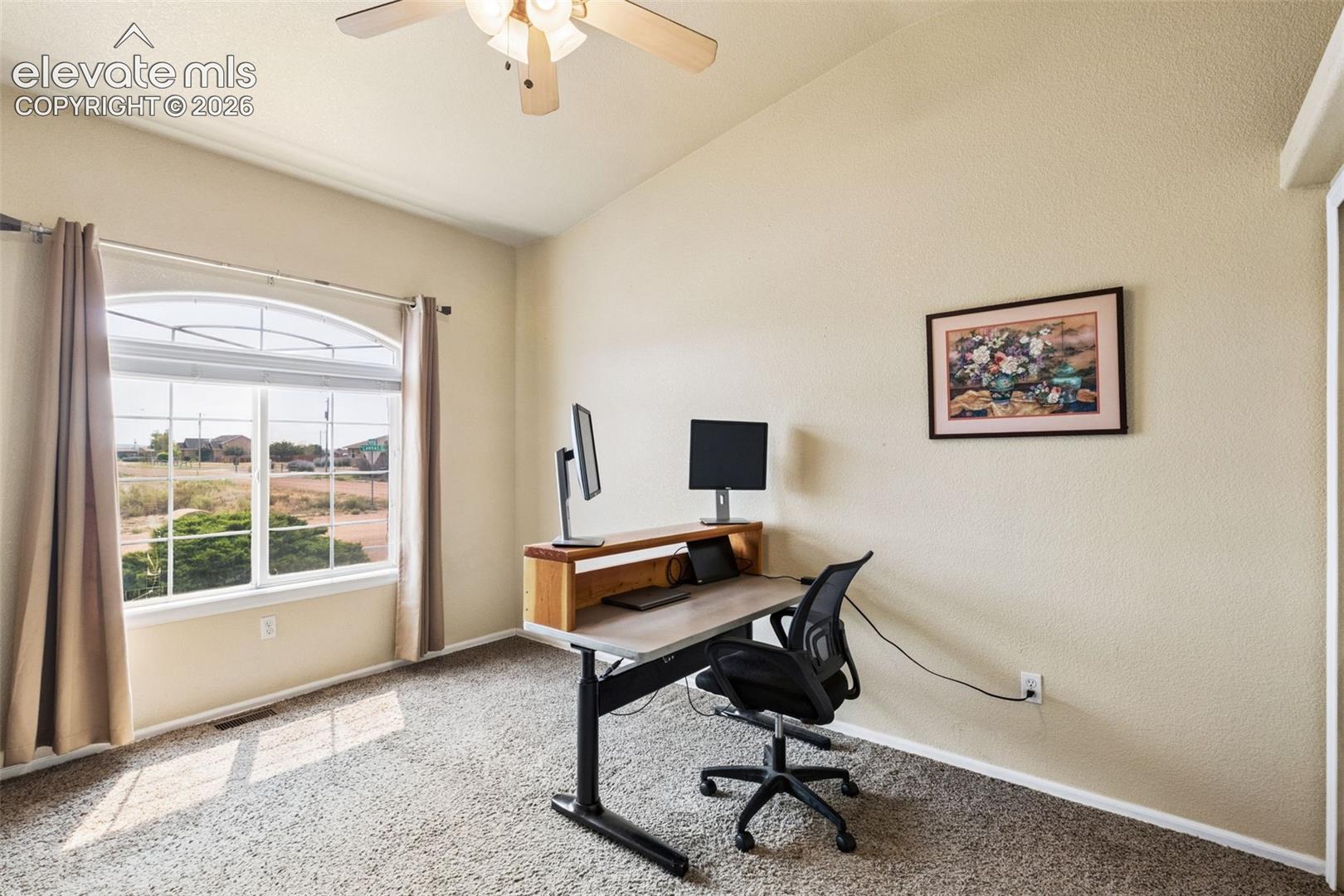 Vaulted ceiling featuring a central lighted ceiling fan, neutral carpeting, and an arched window