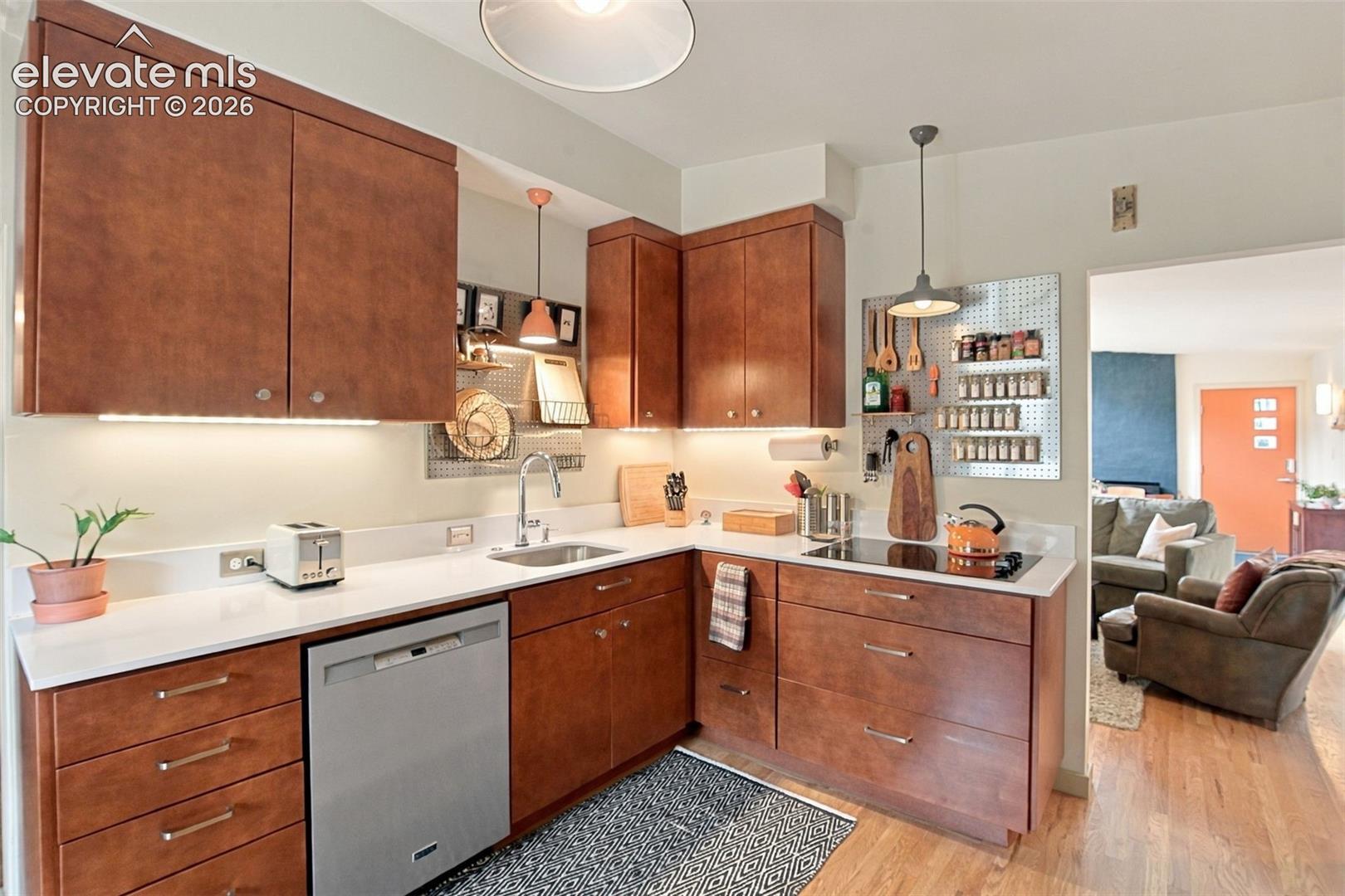 Kitchen featuring stained wood cabinetry, white solid-surface countertops, an undermount stainless steel sink, integrated stainless steel dishwasher, and metallic pendant lighting