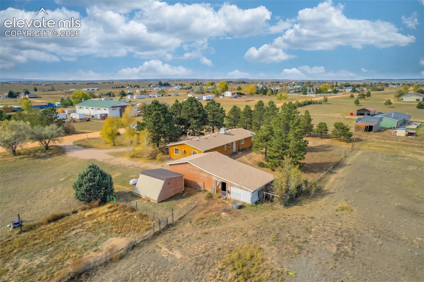 Expansive rural acreage featuring a residence, multi-purpose outbuildings, mature evergreen trees, and perimeter fencing