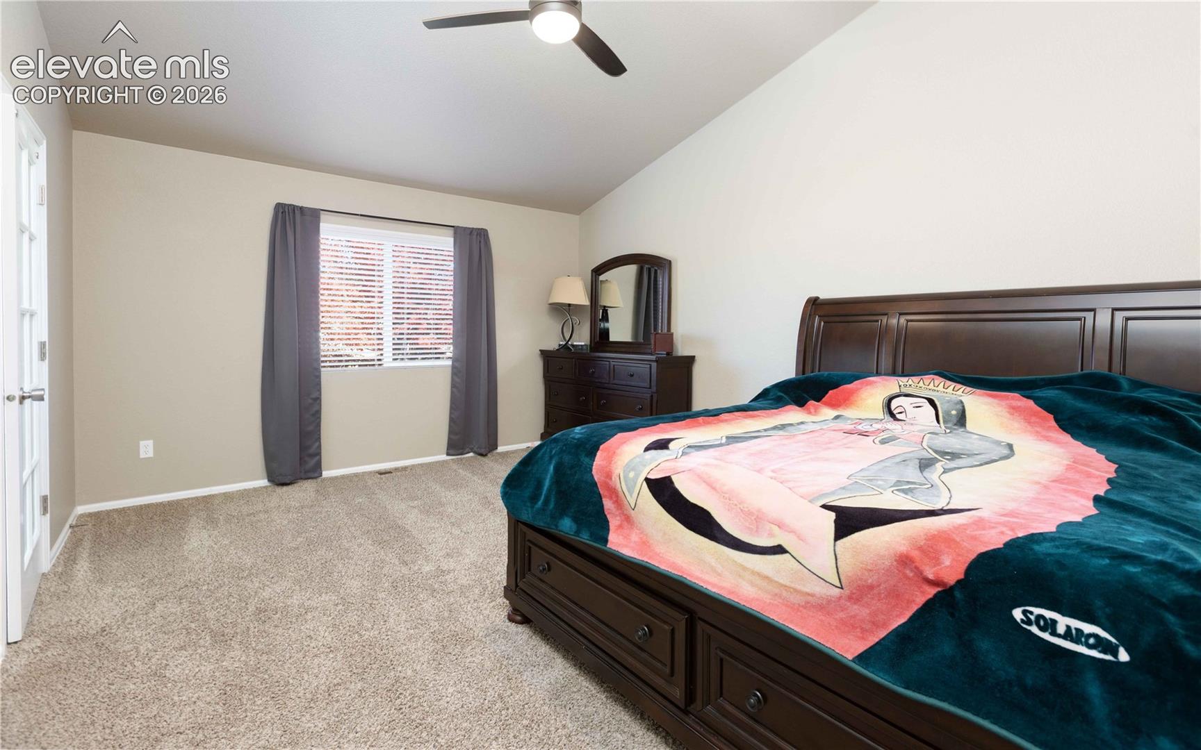 Spacious room featuring neutral wall paint, carpeting, vaulted ceiling, a ceiling fan with integrated lighting, and a multi-pane glass door