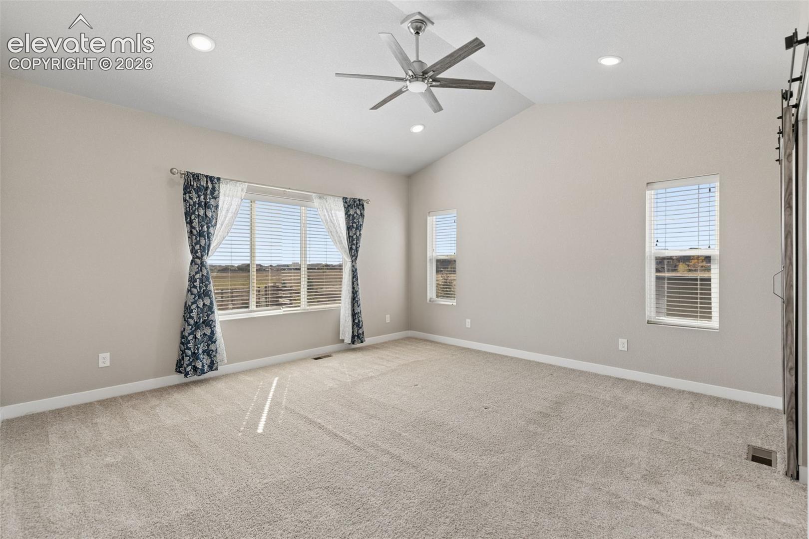Vaulted ceilings featuring recessed lighting and a brushed-metal ceiling fan, neutral carpeting, and a sliding barn door
