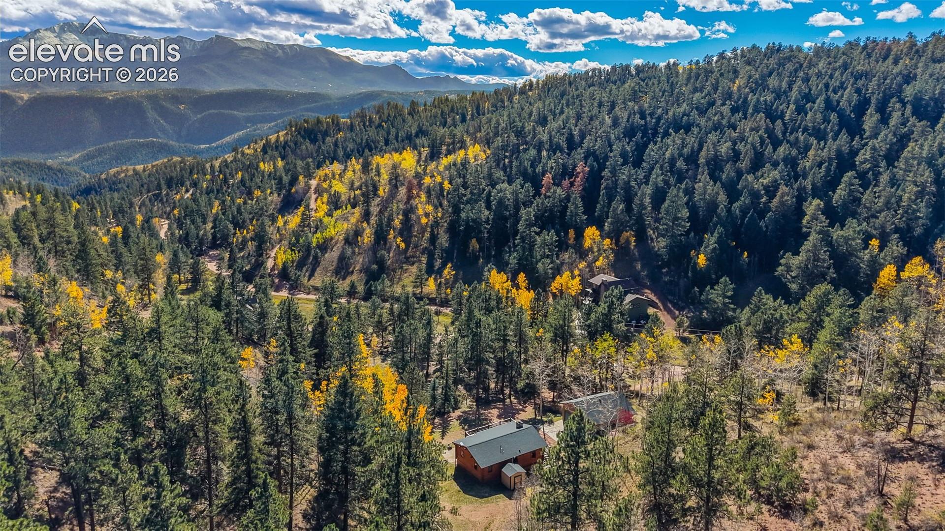 Aerial perspective featuring a multi-structure property nestled within a densely wooded landscape and mountain terrain