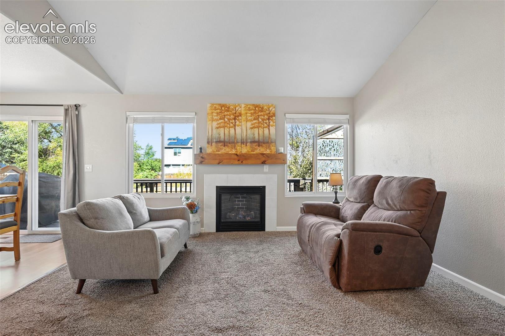 Living area featuring a vaulted ceiling, fireplace with tile surround, wood-beam mantel, and sliding glass door access to the exterior