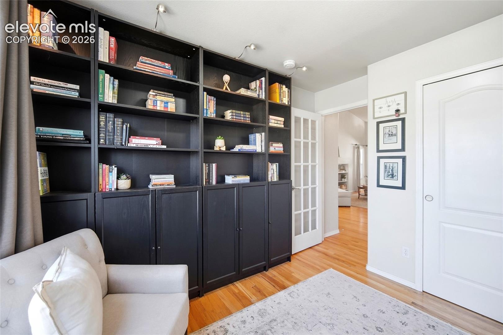 Built-in shelving with lower cabinetry, track lighting, hardwood flooring, and French doors with privacy glass