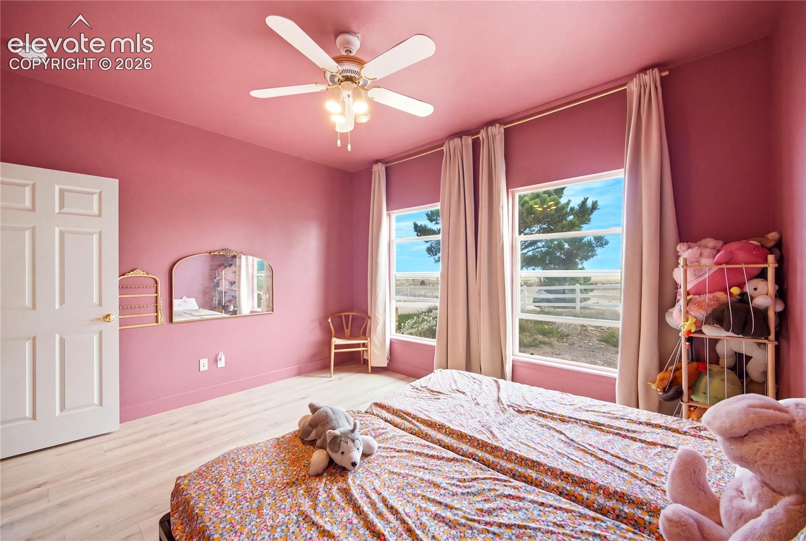 Interior space featuring light-toned wood-finish flooring, dual windows, a central ceiling fan with integrated lighting, and a mounted decorative mirror