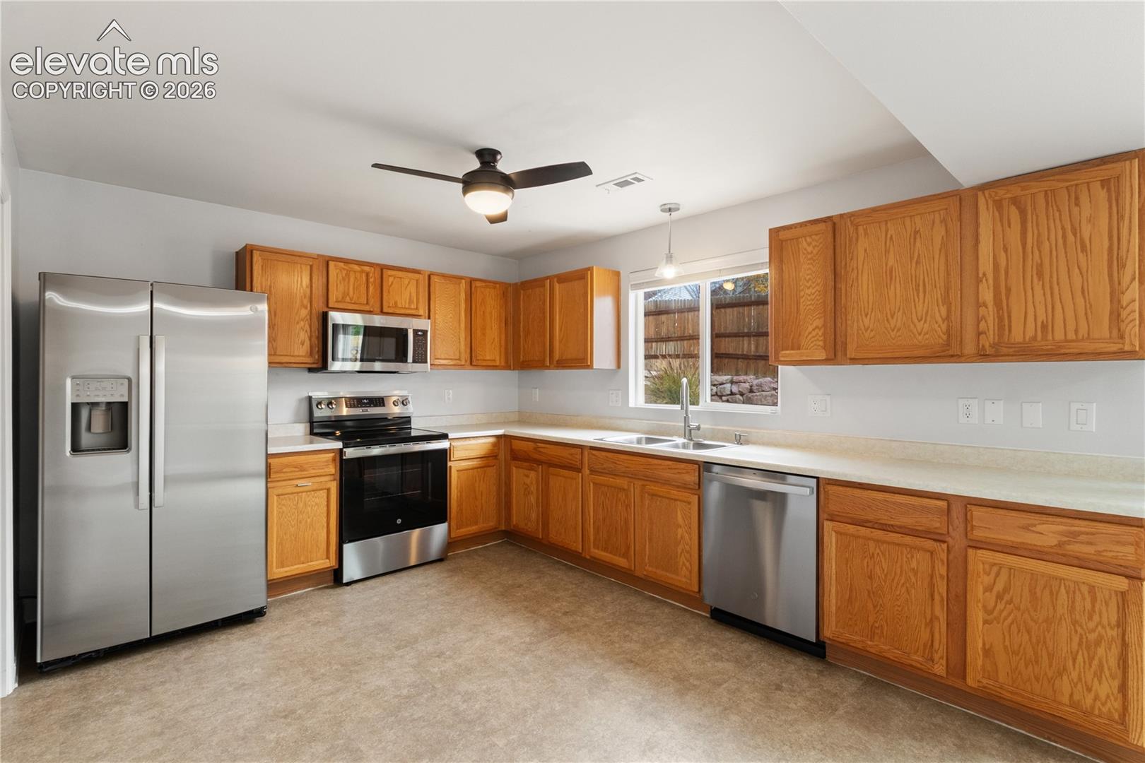 Kitchen featuring wood cabinetry, stainless steel appliances, neutral countertops, a double-basin sink, and a ceiling fan