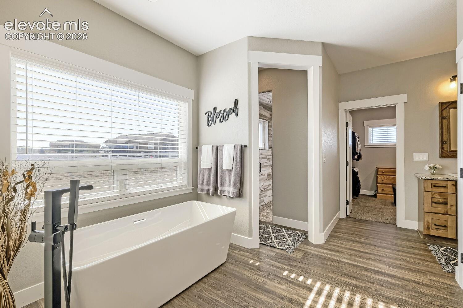 Freestanding soaking tub with floor-mounted faucet, wood-finish flooring, and recessed lighting