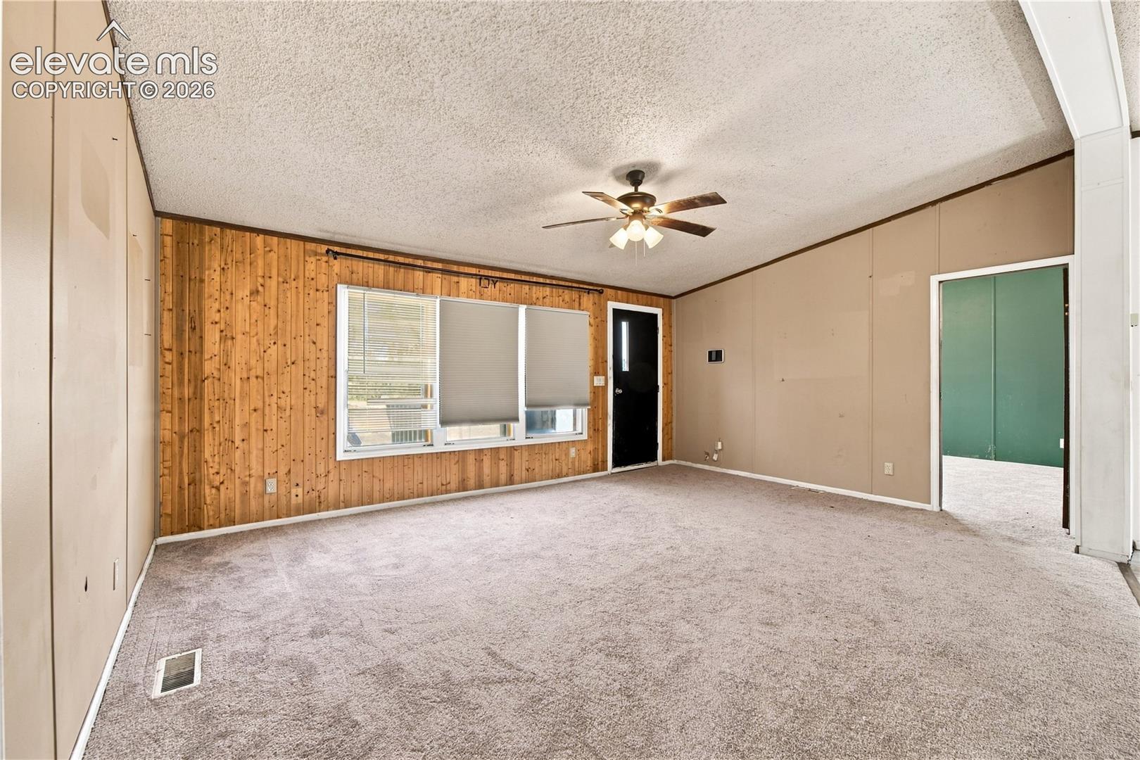 Carpeted flooring, wood paneling, ceiling fan, natural light, and a dark-paneled door