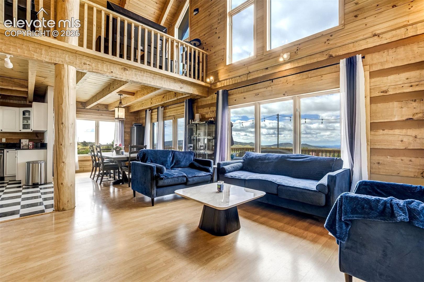 Expansive living area featuring soaring ceilings with exposed wood beams, a second-story interior balcony, and large windows showcasing a distant mountain range