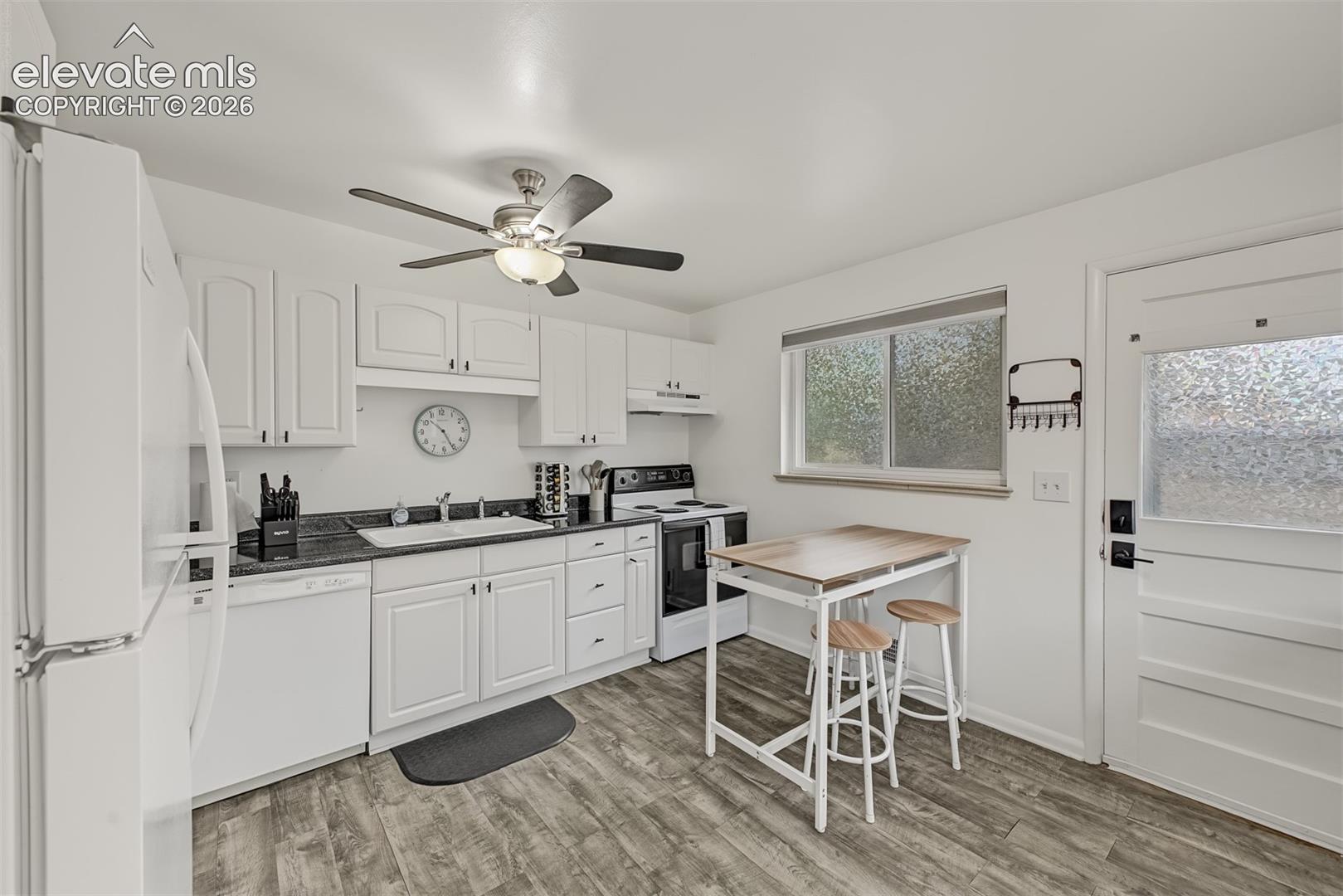 Kitchen featuring white cabinetry, dark stone-finish countertops, wood-finish flooring, a ceiling-mounted light and fan fixture, and a glass-paneled exterior door