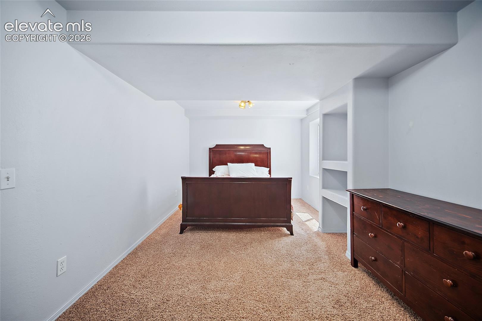 Carpeted room with recessed wall shelving, white painted walls, and a ceiling-mounted light fixture