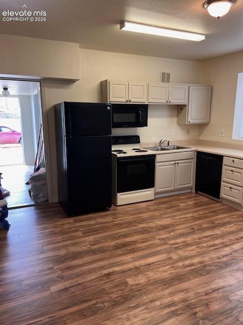 Kitchen featuring wood-finish flooring, white cabinetry, solid-surface countertops, and black appliances including a refrigerator, dishwasher, and over-the-range microwave