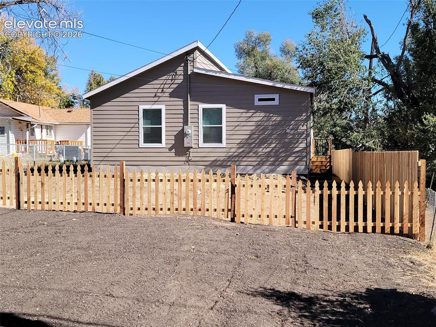 Exterior featuring horizontal lap siding, a gabled roofline, double-hung windows, and a wood picket fence enclosing a level ground area