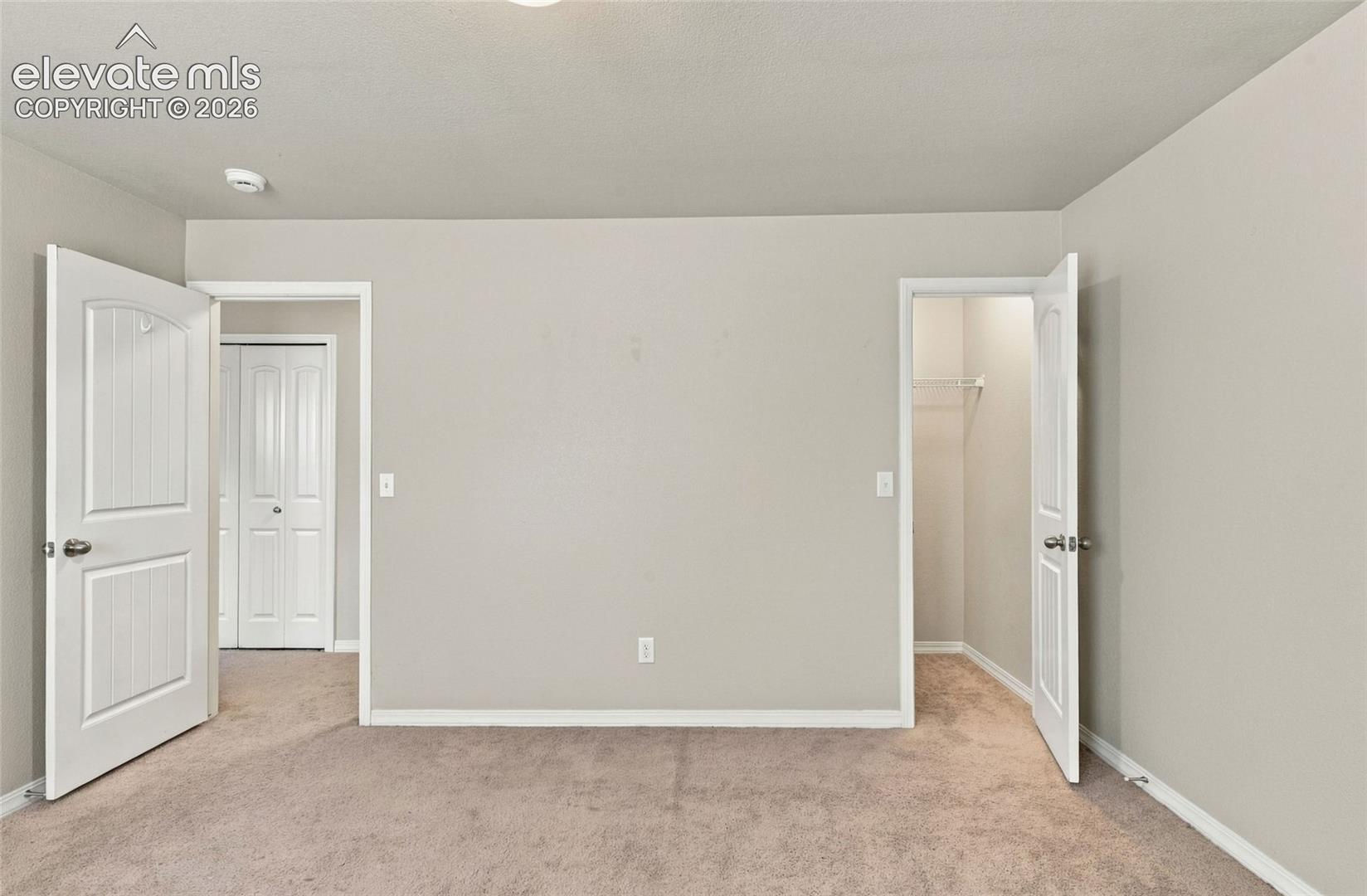 Neutral-toned interior space featuring beige carpeting, two-panel interior doors, and a walk-in closet with integrated shelving