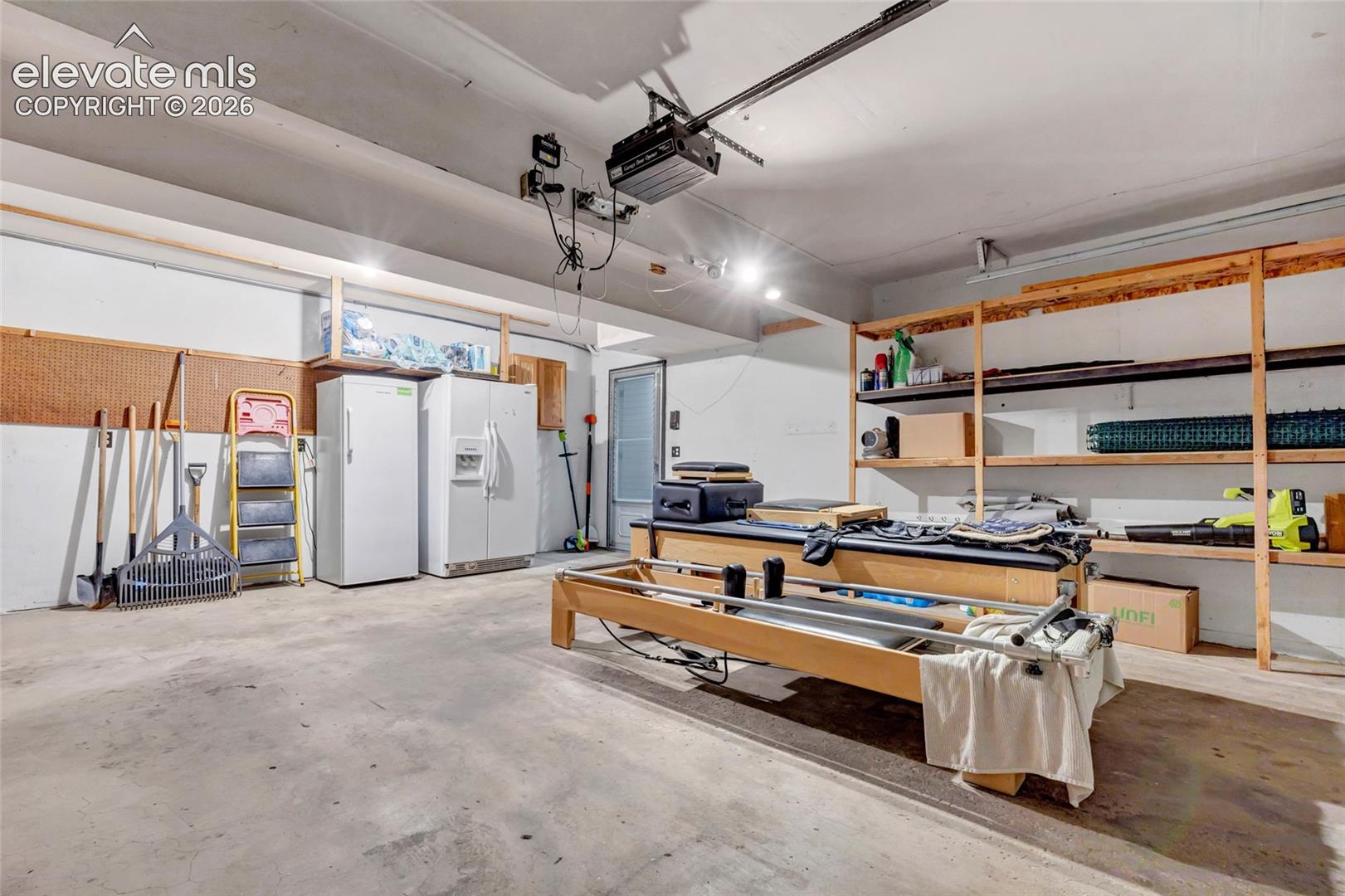 Spacious garage featuring a concrete floor, overhead lighting, garage door opener, built-in shelving, and a service door