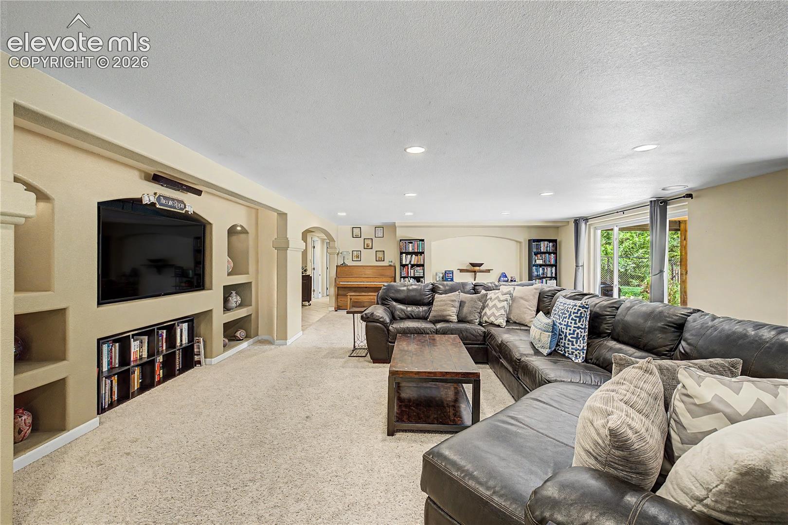 A built-in "Theatre Room" media wall, complete with custom display niches, anchors this expansive lower-level living area, where a large window brings in unexpected natural light for a basement space.