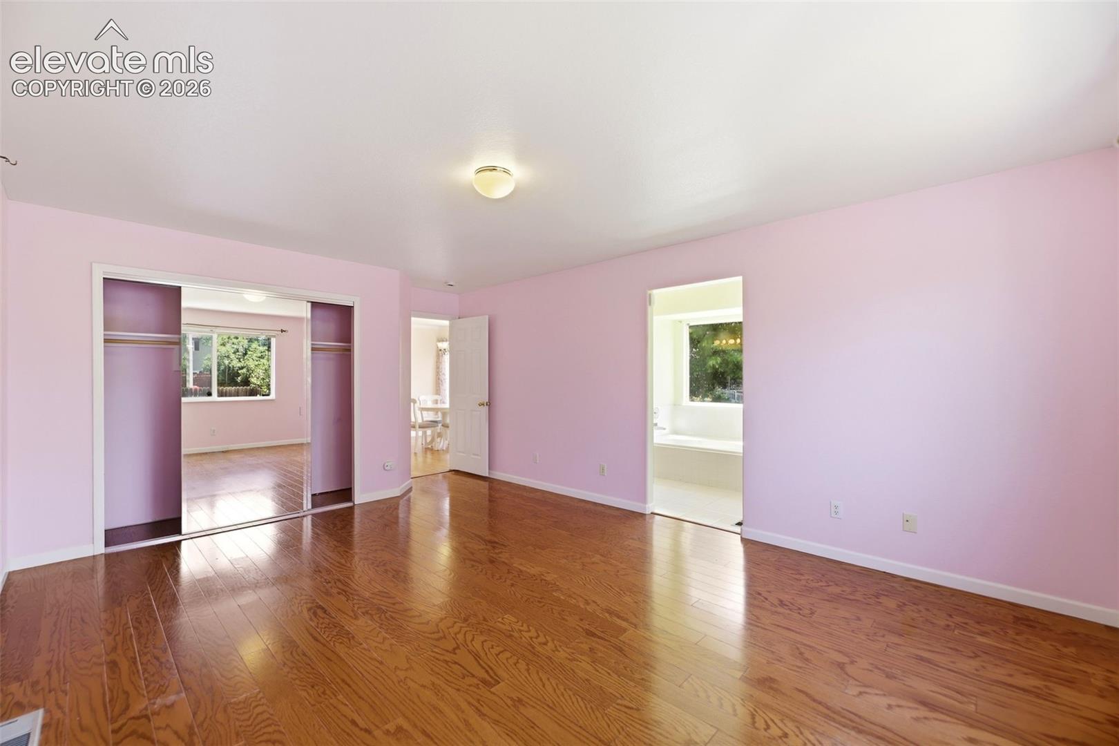 Spacious room featuring hardwood flooring, light pink walls, and a ceiling-mounted light fixture