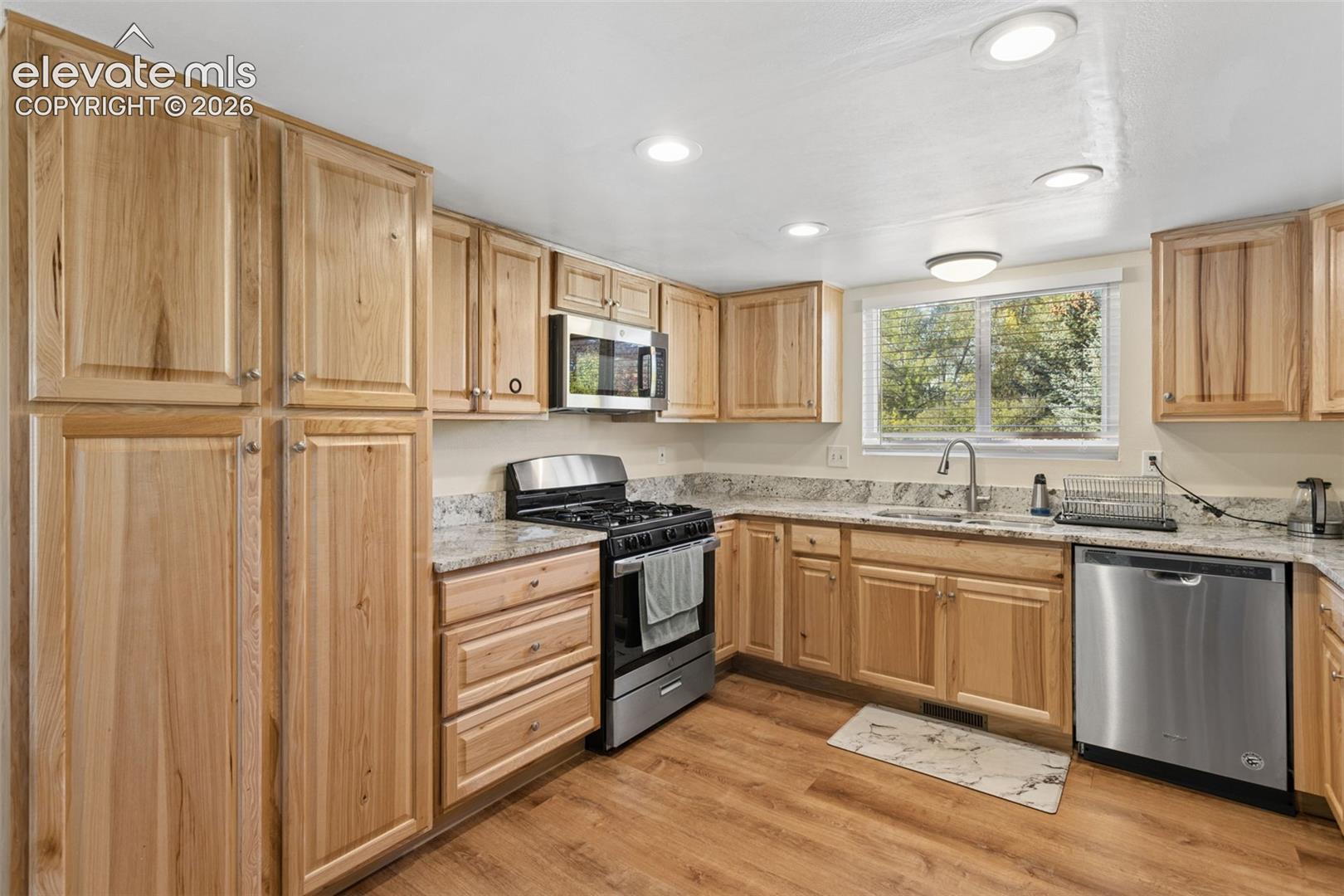 Kitchen featuring wood-finish flooring, light wood cabinetry, stone countertops, and stainless steel appliances
