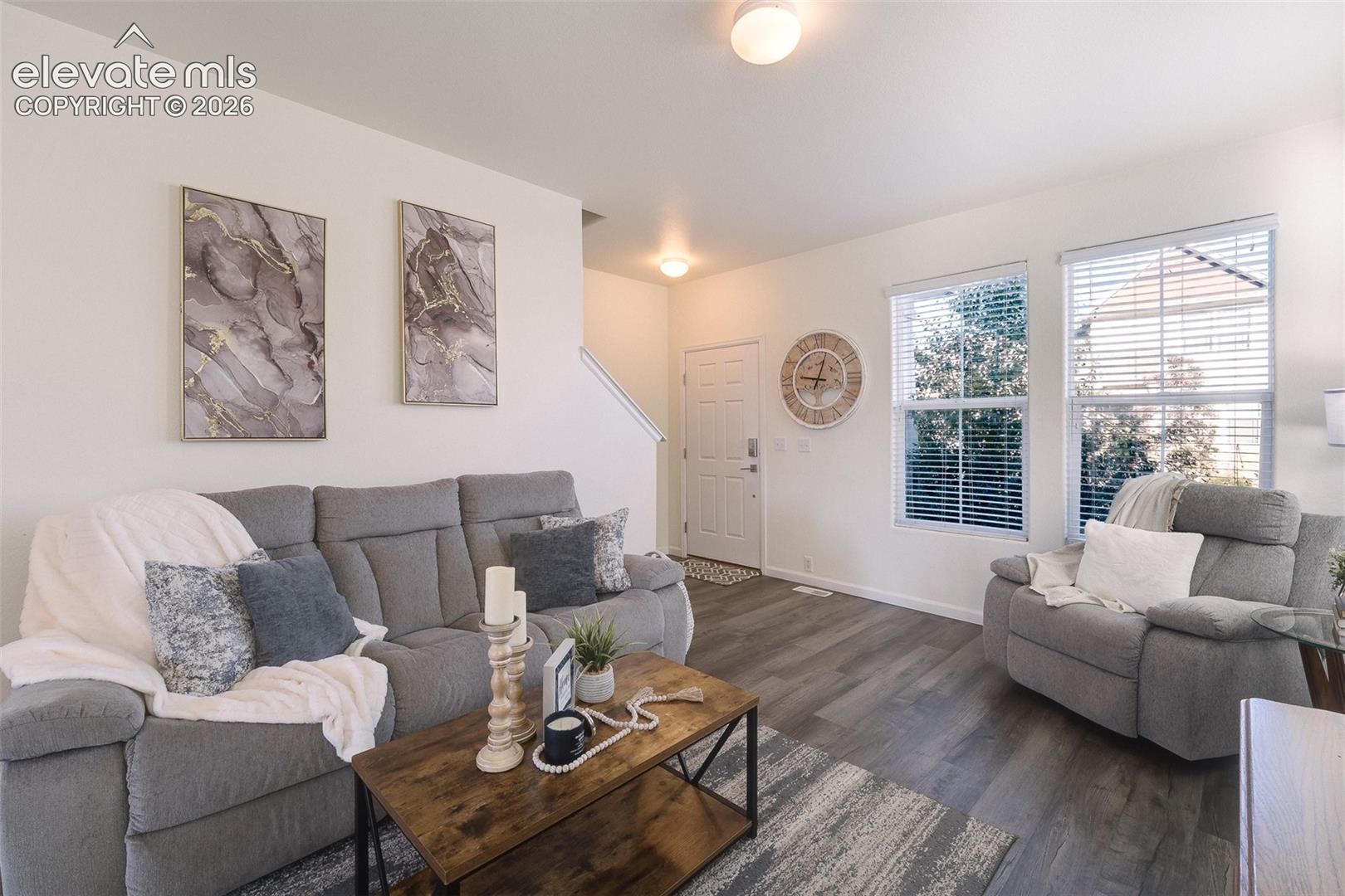 Living area featuring wood-finish flooring, two large windows with blinds, a white entry door, and recessed lighting
