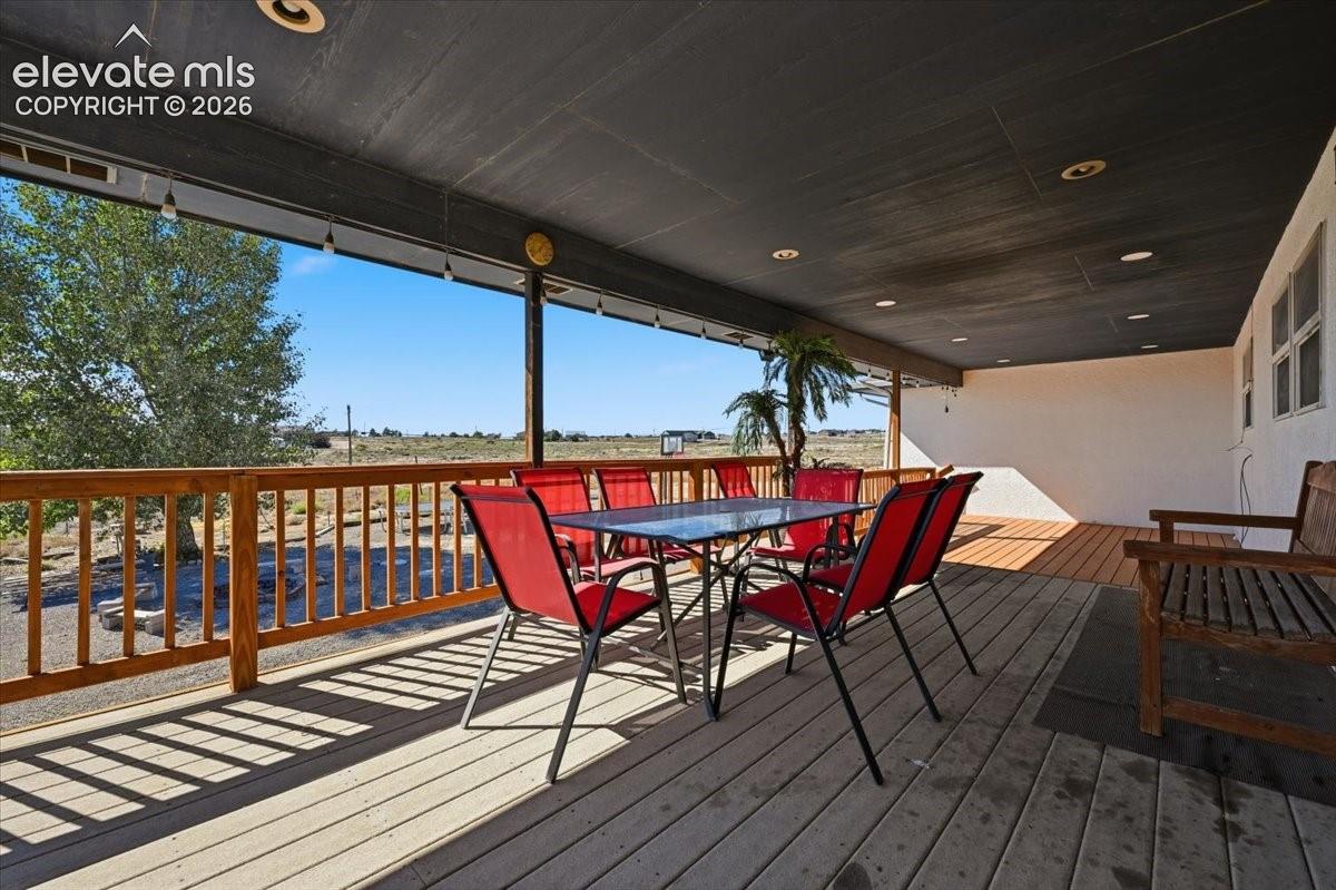 Covered outdoor deck featuring a composite wood-tone surface, recessed ceiling lighting, and wood-finish railing
