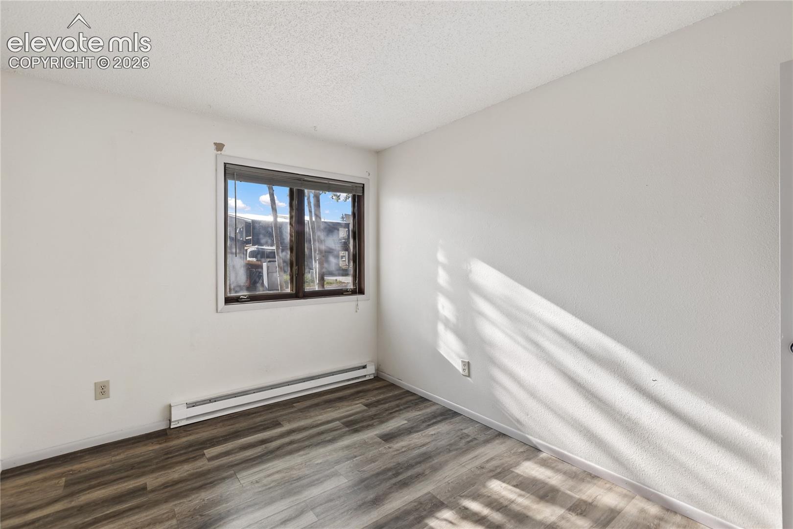 Window with dark trim, baseboard heating unit, and wood-finish flooring