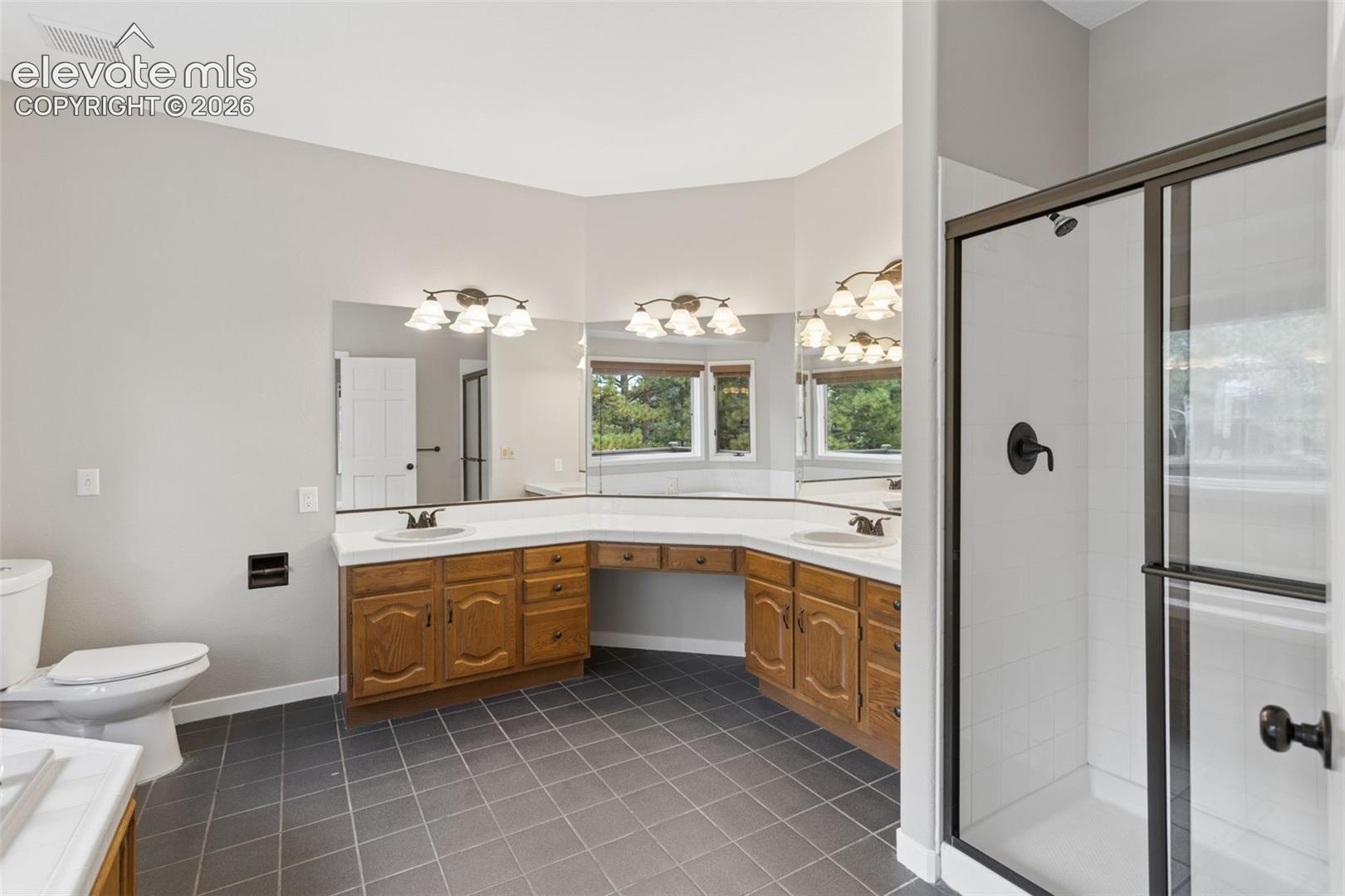 Dual vanities with integrated sinks, expansive vanity mirror, corner shower with dark-framed glass enclosure, and tiled flooring