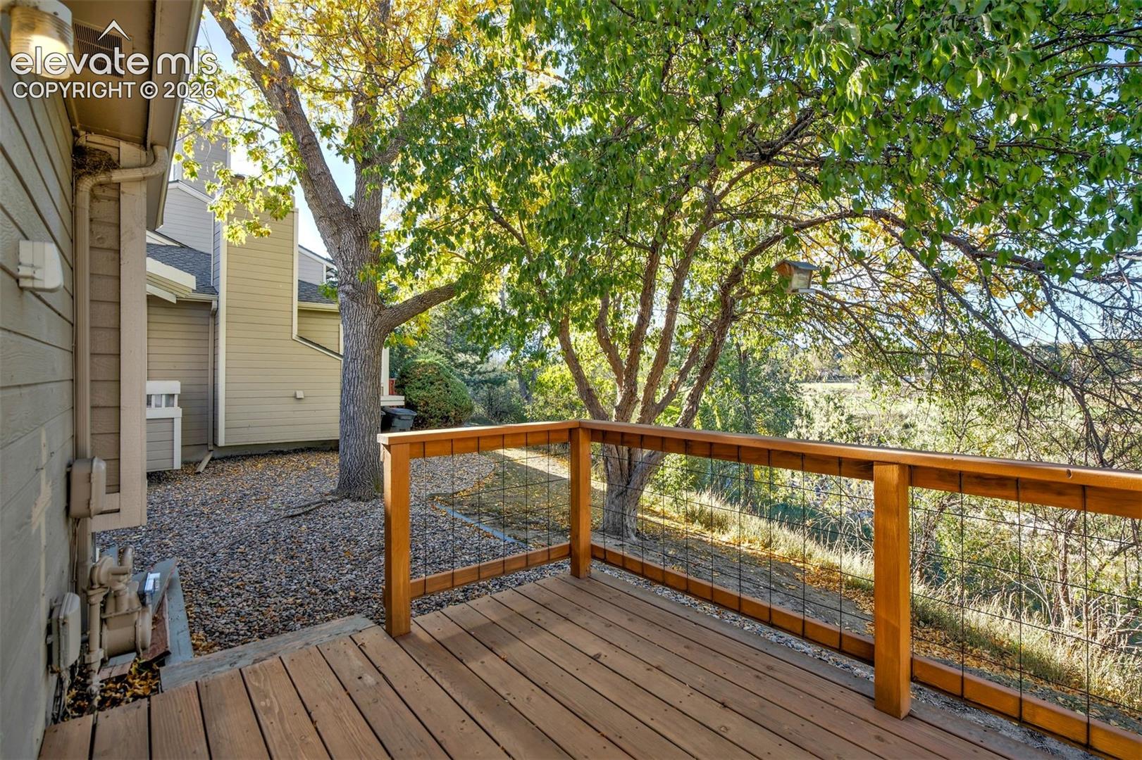 Elevated wood deck featuring a wire-grid railing and mature trees