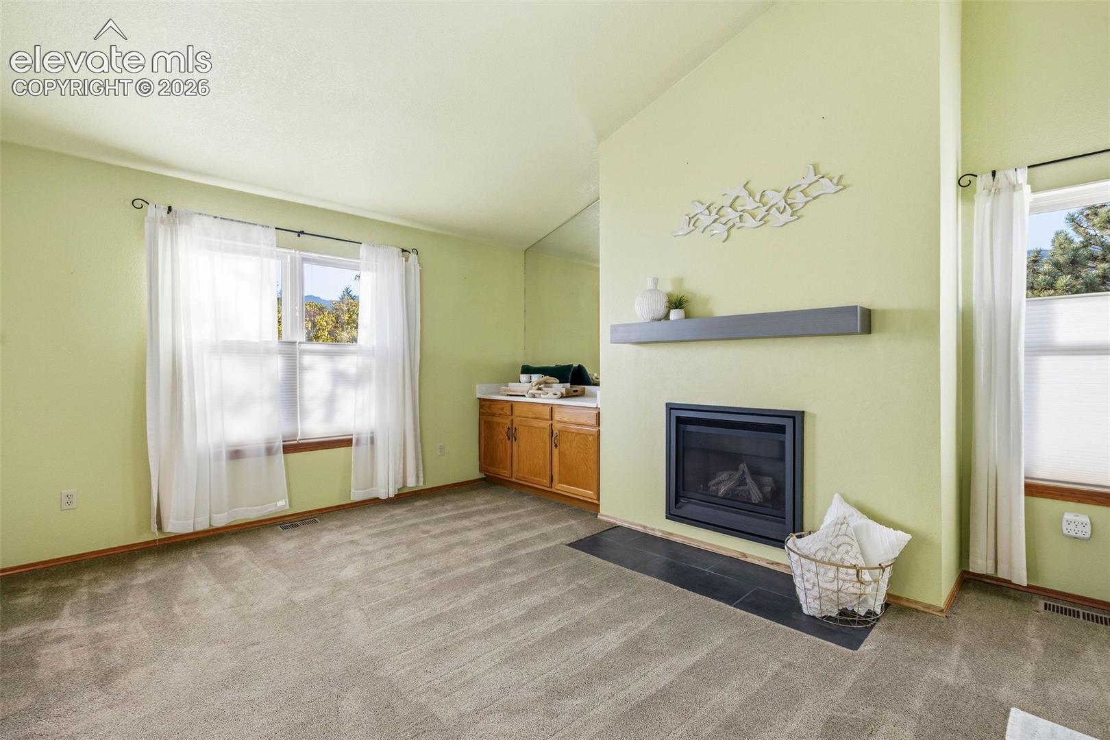 Vaulted ceilings, fireplace with a slate-tile hearth, floating mantel, and built-in cabinetry with stone-surface countertop