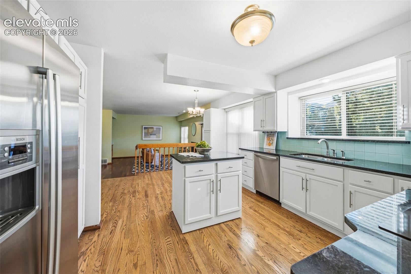Kitchen featuring white shaker-style cabinetry, dark stone countertops, a central island, stainless steel appliances, and wood-finish flooring