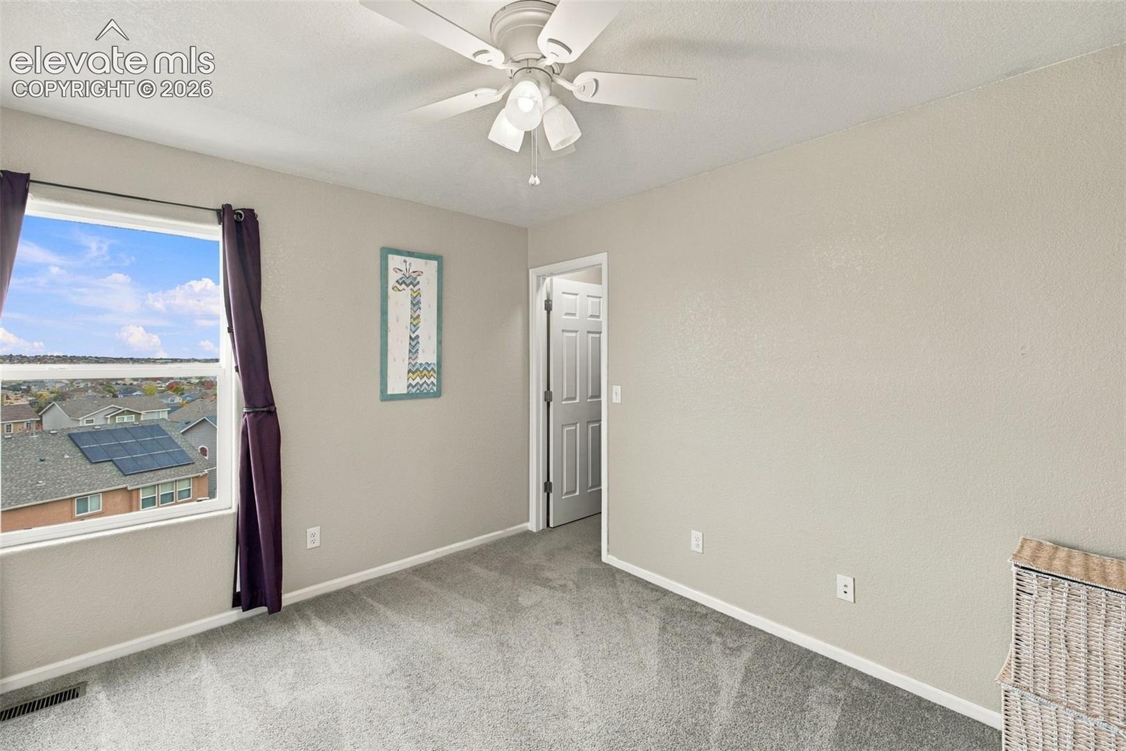 Neutral-toned interior space featuring neutral wall-to-wall carpeting, a multi-blade ceiling fan with integrated light fixture, and a large single-pane window