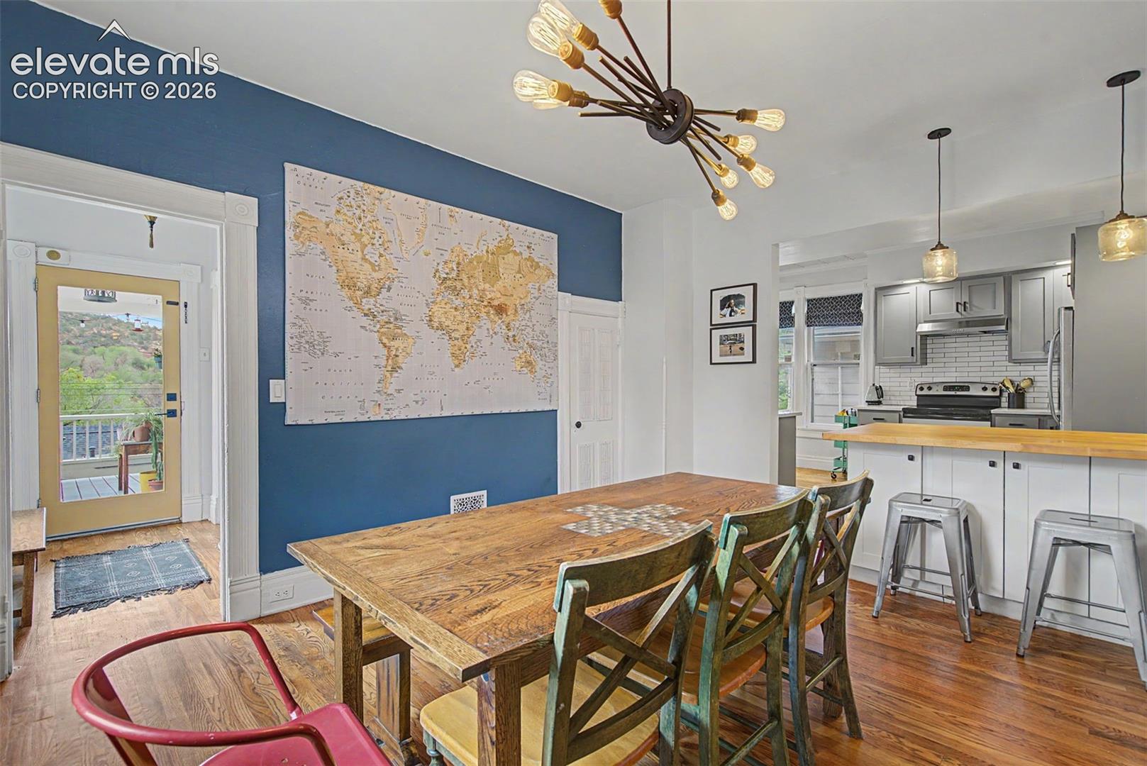 Open-concept dining area featuring hardwood flooring, a modern chandelier, and a breakfast bar/ kitchen island