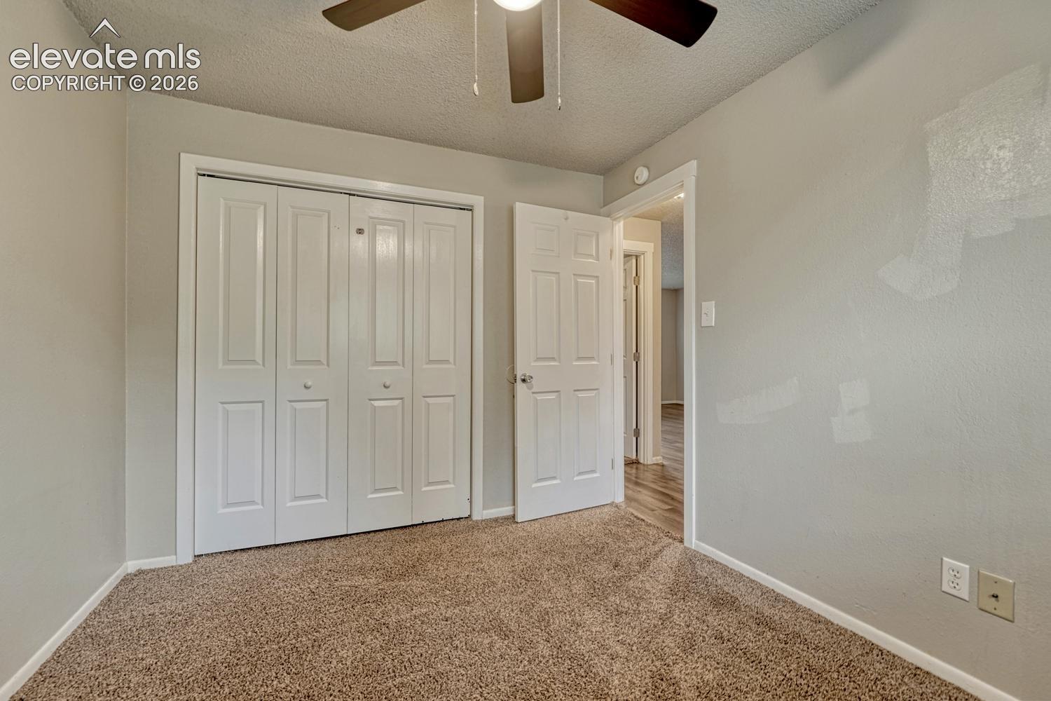 Carpeted flooring, bi-fold closet doors, ceiling fan with light fixture, and wood-finish flooring visible through doorway