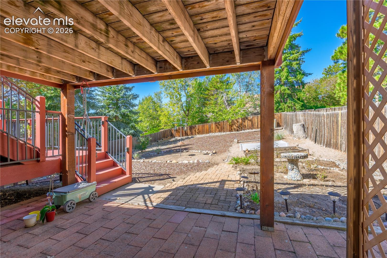 Covered patio with brick pavers, wood deck with stairs, wood lattice, and fenced yard